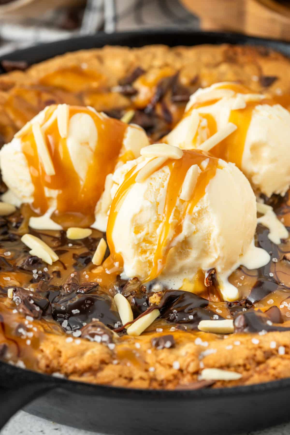 Melting ice cream, molten caramel, and crisp skillet-cookie edges make this whole dessert feel wildly excessive in the best way. Gooey salted caramel skillet cookie topped with melting vanilla ice cream, caramel sauce, chocolate drizzle, flaky sea salt, and chocolate chunks in a cast iron skillet.