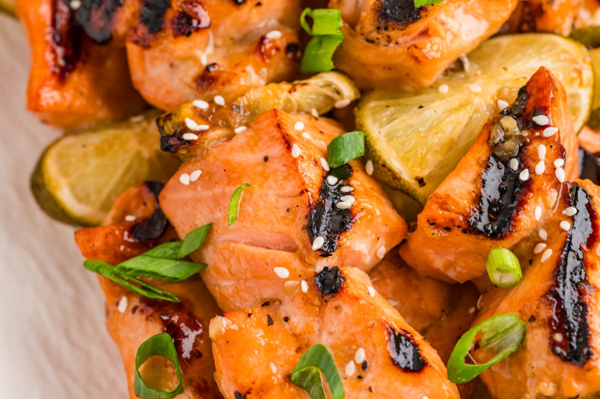 Close-up of grilled honey soy lime salmon skewers with caramelized char, sesame seeds, green onions, and grilled lime slices.