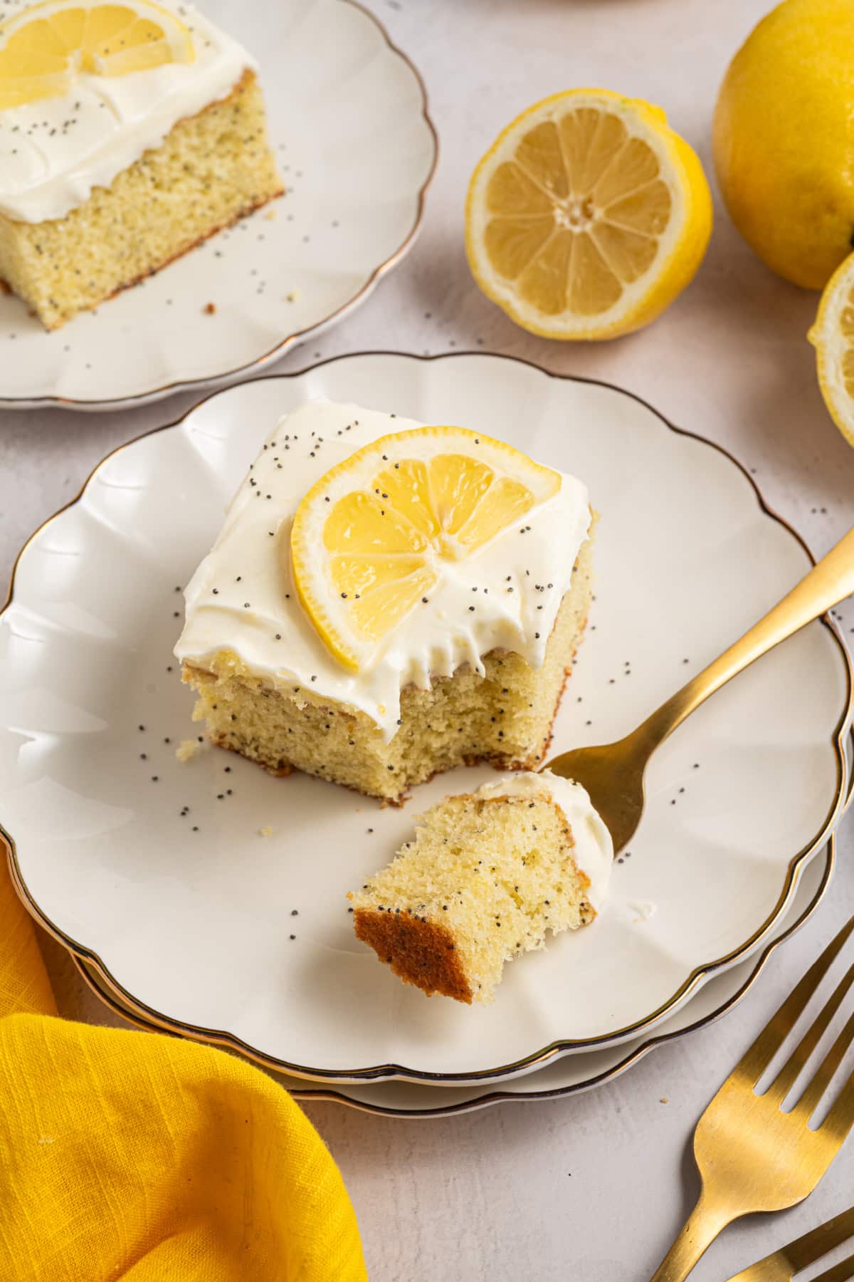 Lemon poppy seed cake with cream cheese frosting and a bite on a fork Lemon poppy seed cake with cream cheese frosting on a plate with a bite taken and a fork holding a piece