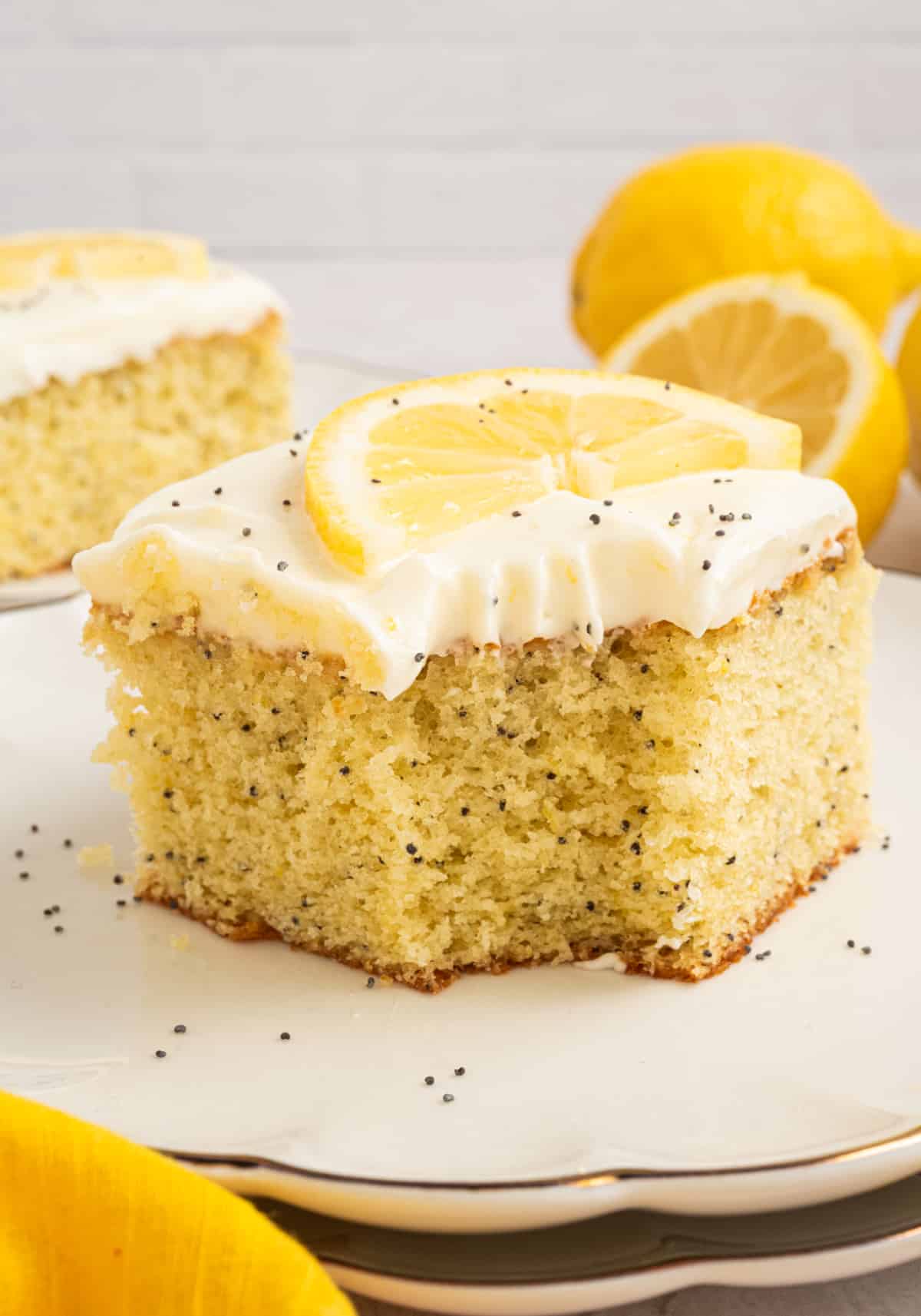 Lemon poppy seed cake with cream cheese frosting and fresh lemon slice Lemon poppy seed cake slice with cream cheese frosting, topped with a fresh lemon slice and poppy seeds on a white plate