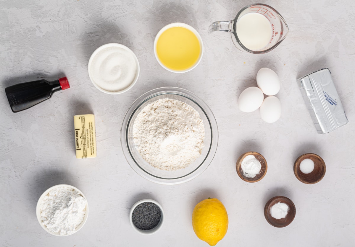 Ingredients for lemon poppy seed cake arranged for baking Ingredients for lemon poppy seed cake including flour, sugar, eggs, lemon, poppy seeds, milk, and butter arranged on a light surface