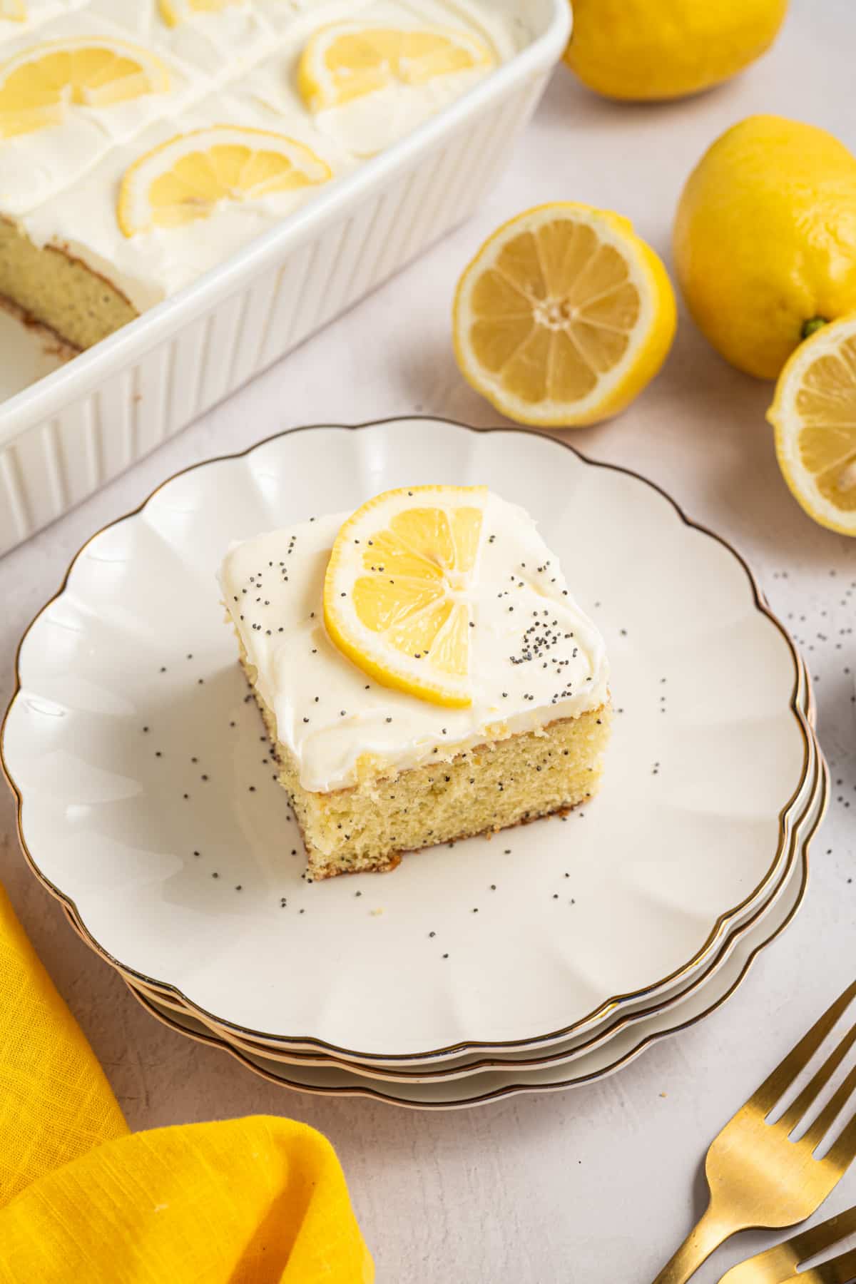 Lemon poppy seed cake slice with cream cheese frosting on a plate Lemon poppy seed cake with cream cheese frosting served on a white plate with lemon slice garnish