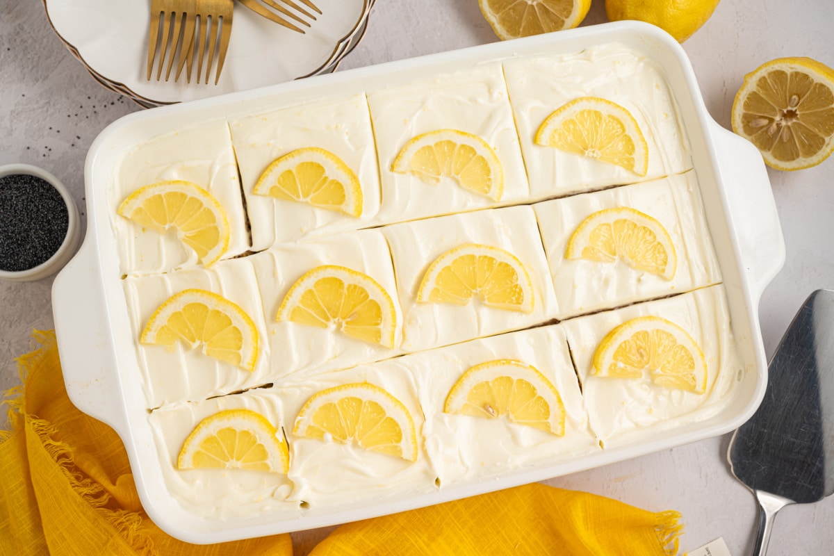 Lemon poppy seed sheet cake with cream cheese frosting cut into squares Lemon poppy seed sheet cake with cream cheese frosting, cut into squares and topped with lemon slices in a baking dish