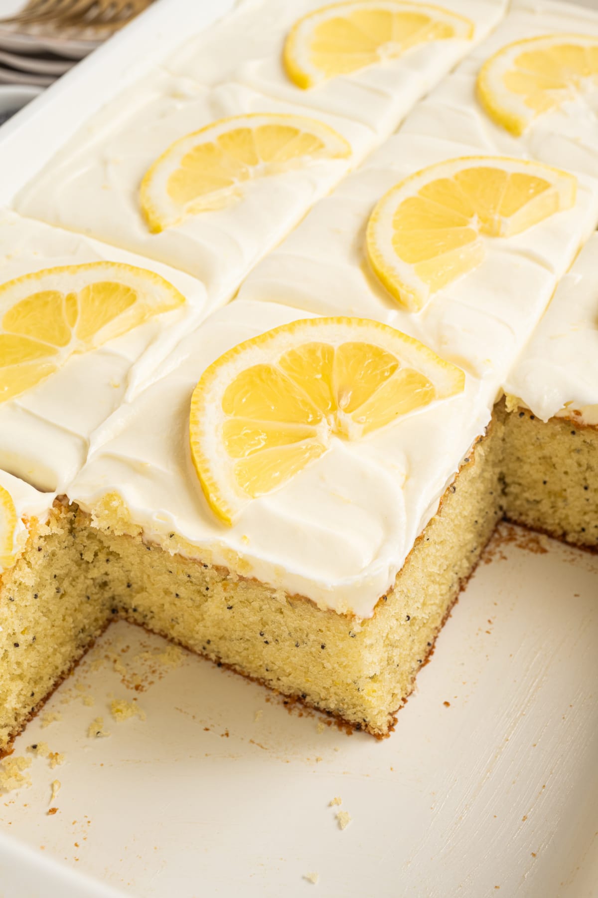 Lemon poppy seed sheet cake with cream cheese frosting and cut corner Close-up of lemon poppy seed sheet cake with cream cheese frosting, showing a cut corner and soft interior crumb