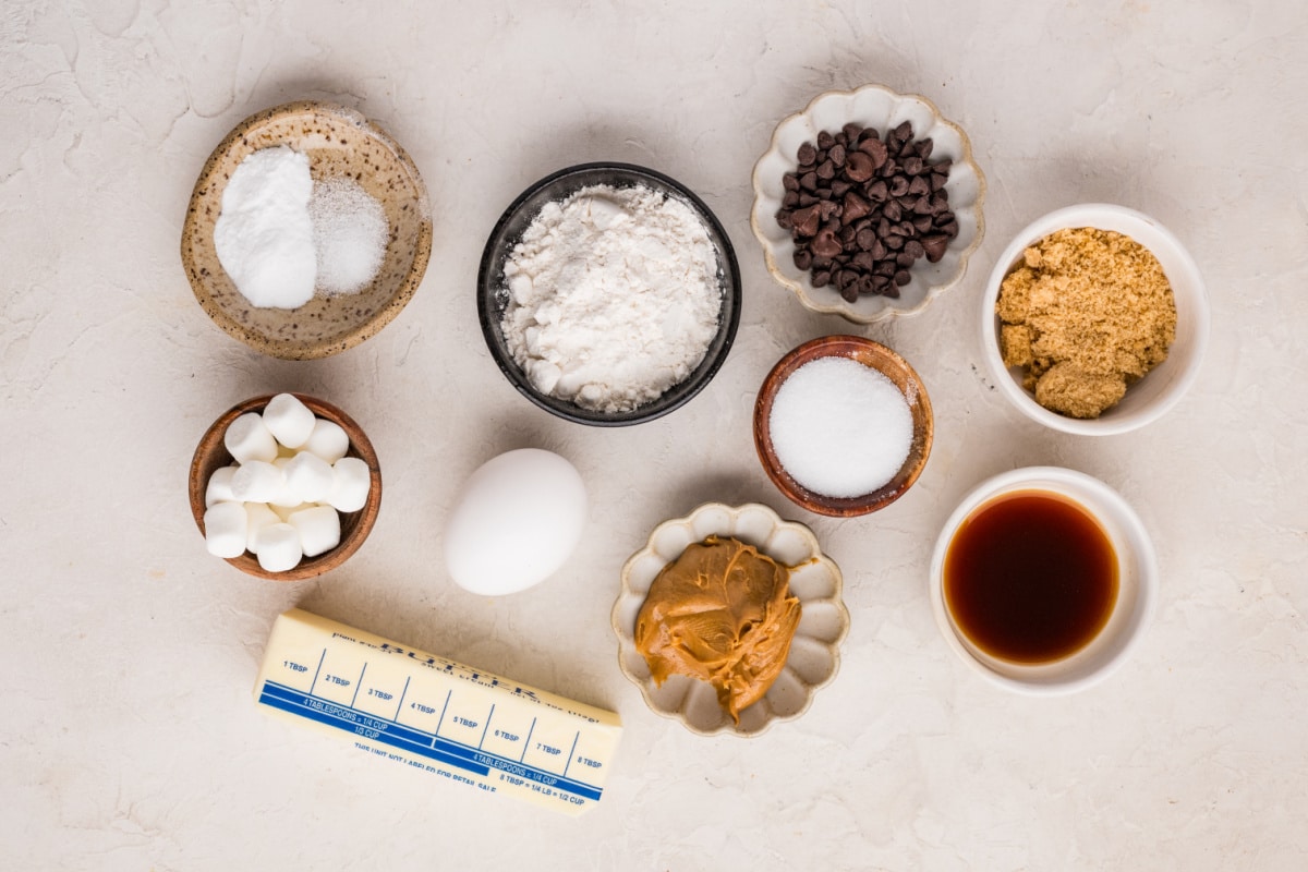 Ingredients for peanut butter marshmallow cookies including peanut butter, mini marshmallows, chocolate chips, flour, butter, brown sugar, and vanilla.