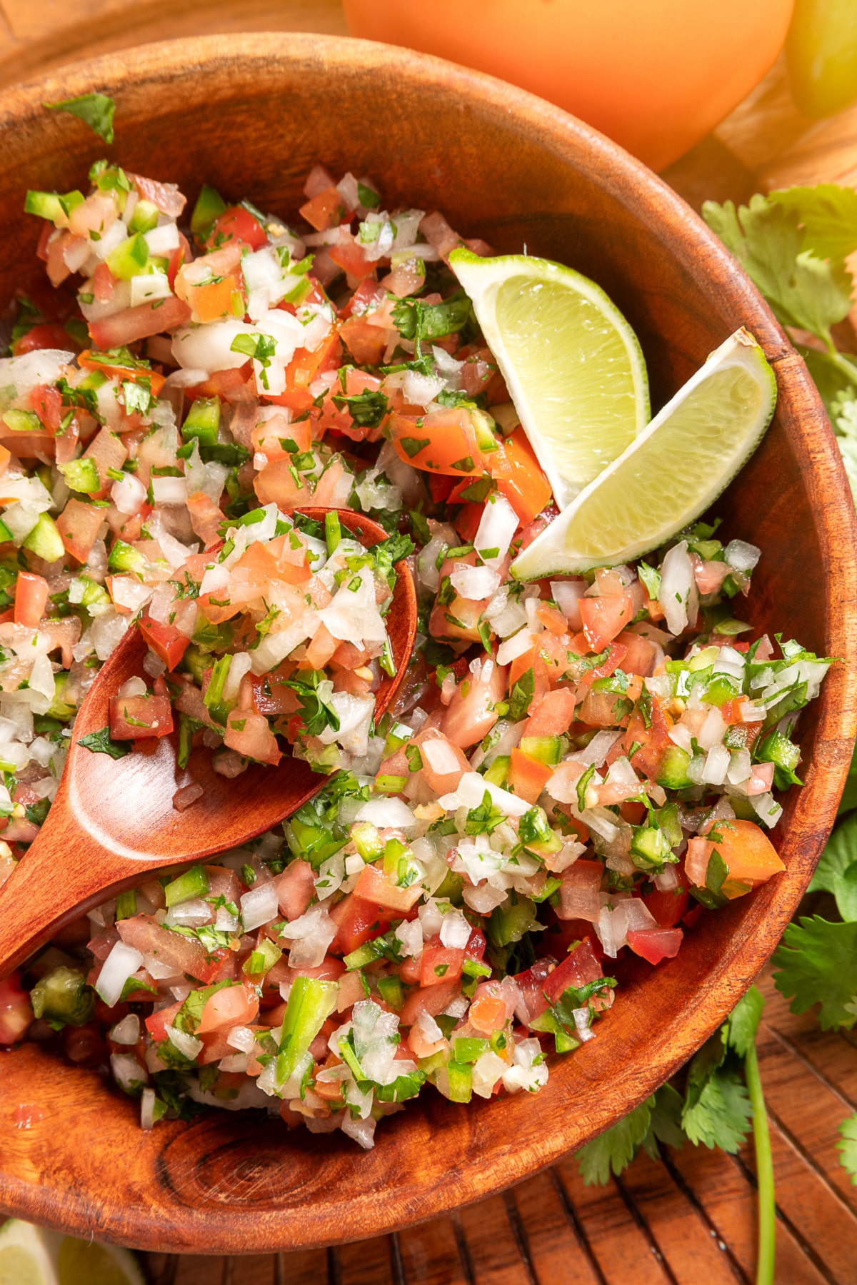 Chunky pico de gallo with diced tomatoes, onion, jalapeño, cilantro, and lime wedges in a wooden bowl