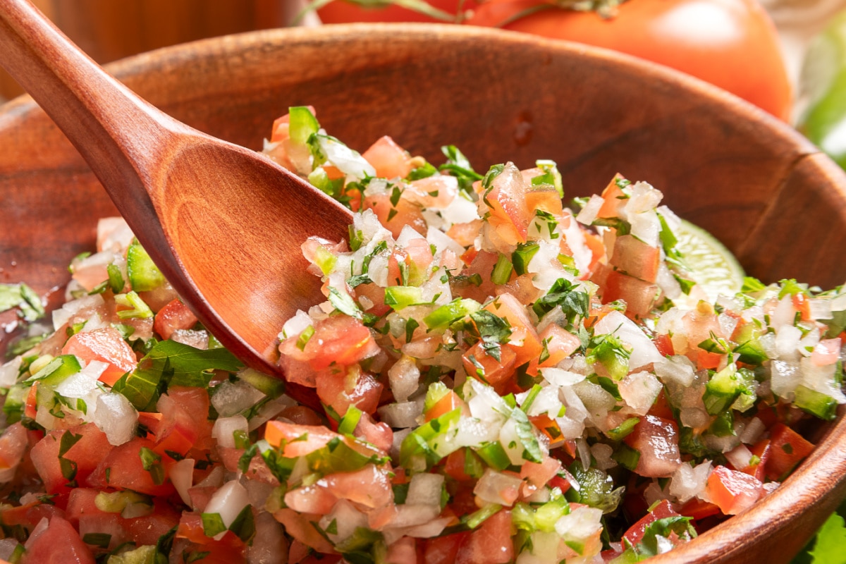 Close-up of chunky pico de gallo with diced tomatoes, onion, jalapeño, cilantro, and a wooden serving spoon