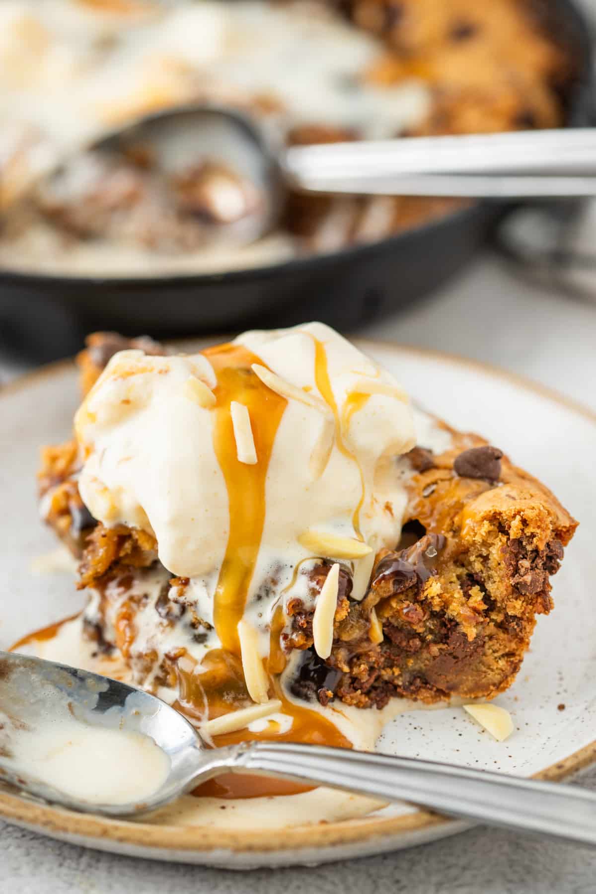 The molten caramel center, melted chocolate, and warm cookie underneath make this feel more like a restaurant dessert than a regular skillet cookie. Slice of salted caramel skillet cookie topped with melting vanilla ice cream, caramel drizzle, chocolate chunks, and molten caramel on a dessert plate.