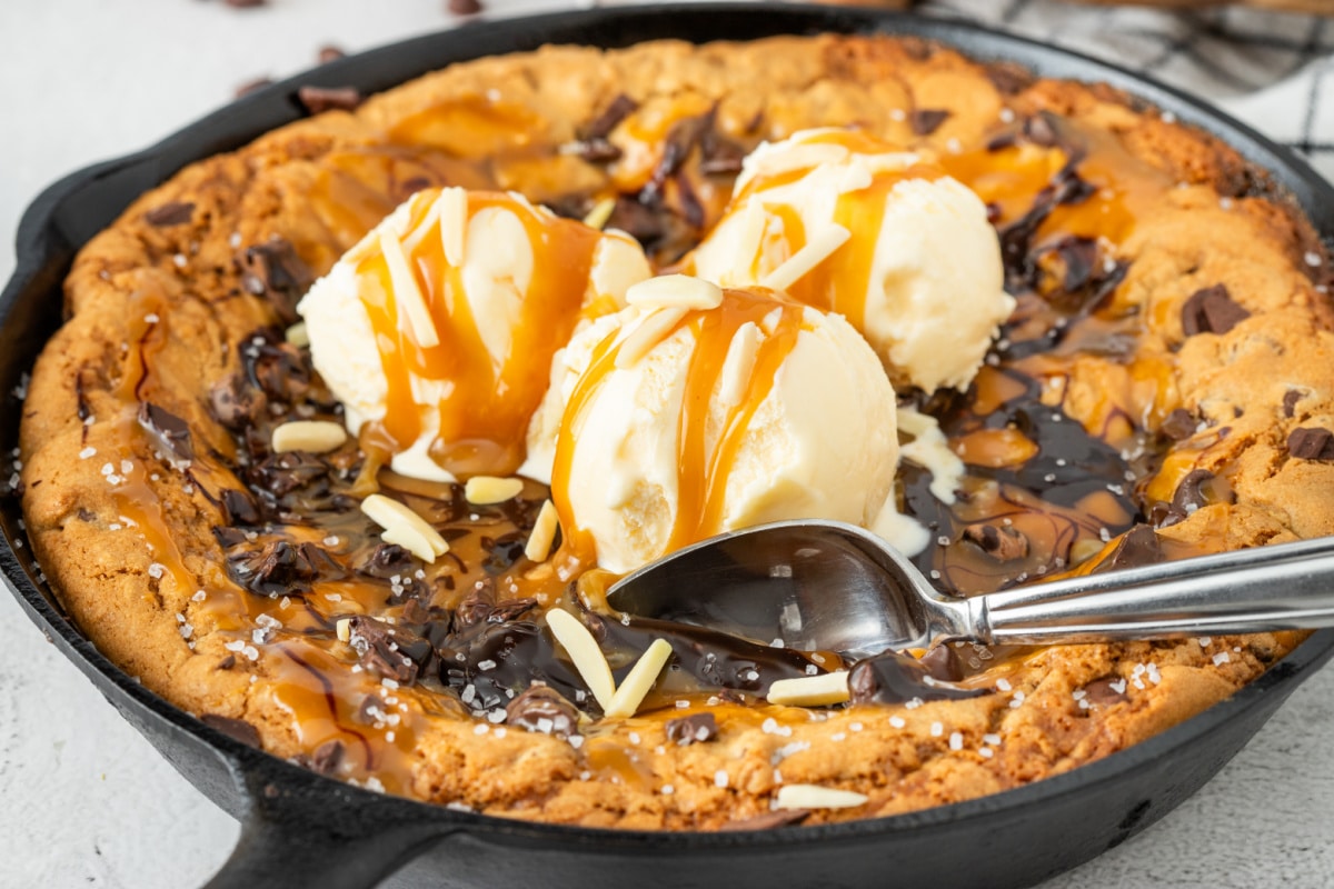 The crisp outer edge, melting ice cream, and molten caramel center are the whole point of this lava-style skillet dessert. Warm salted caramel skillet cookie topped with vanilla ice cream, chocolate drizzle, flaky sea salt, and molten caramel in a cast iron skillet.