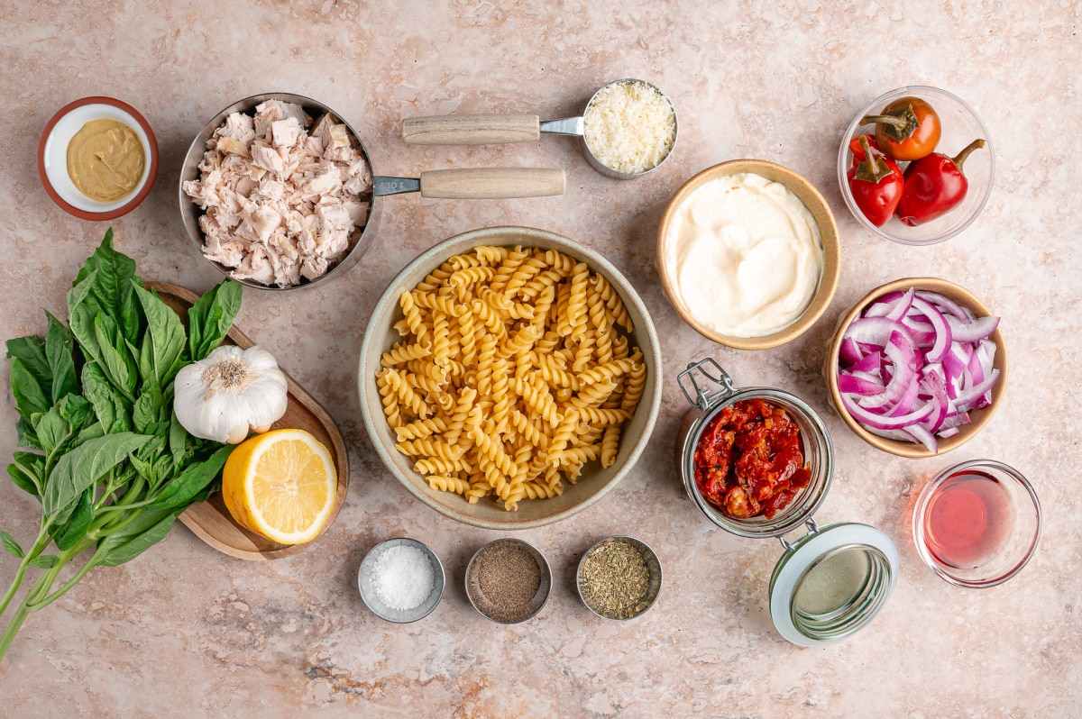 Ingredients for chicken pasta salad with basil, Parmesan, lemon juice, rotini, and sun-dried tomatoes packed in oil Ingredients for Sun-Dried Tomato Chicken Pasta Salad including rotini pasta, rotisserie chicken, basil, lemon, Parmesan, mayonnaise, and oil-packed sun-dried tomatoes