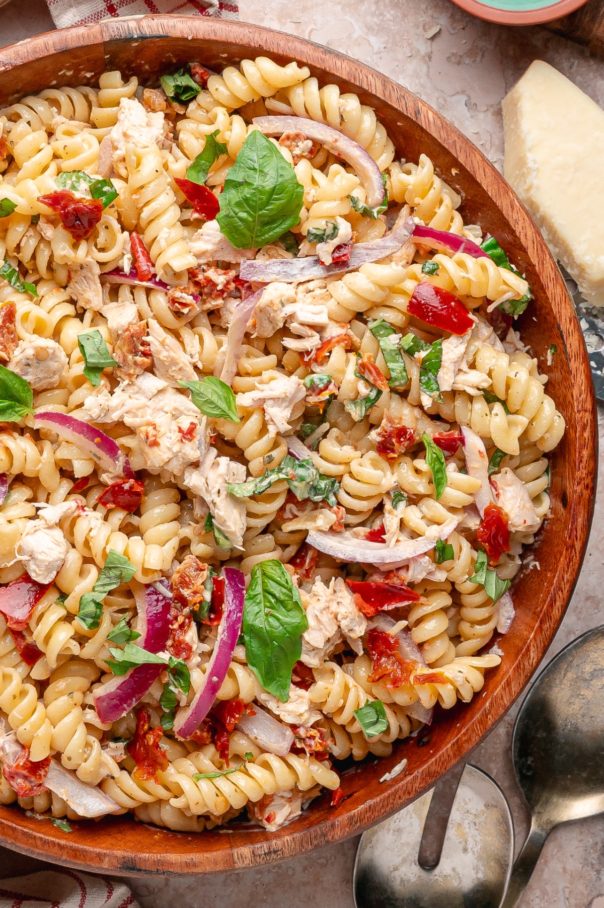 Sun-Dried Tomato Chicken Pasta Salad with basil, rotisserie chicken, and a glossy sun-dried tomato dressing in every bite Sun-Dried Tomato Chicken Pasta Salad with rotini, rotisserie chicken, basil, red onion, roasted red peppers, and Parmesan in a wooden serving bowl