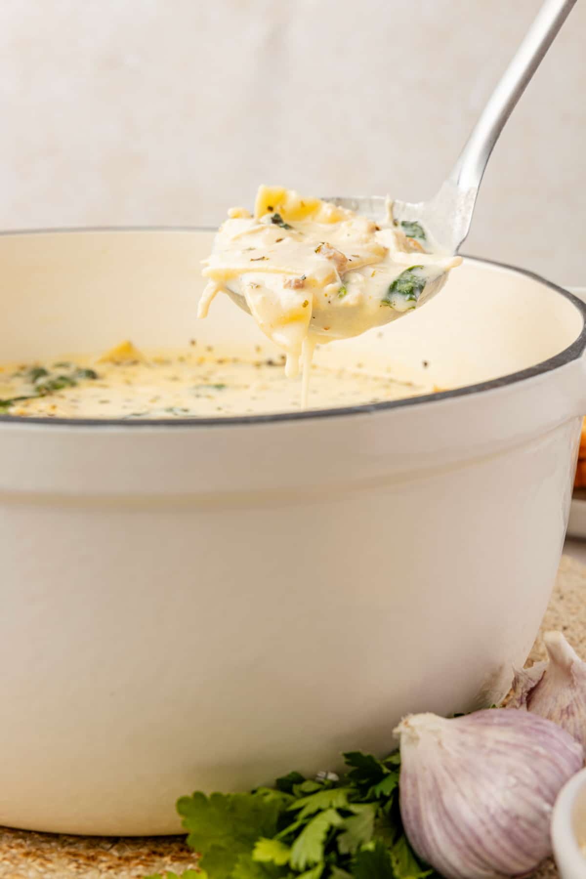 White chicken lasagna soup with ricotta, spinach, sausage, and lasagna noodles lifted from creamy broth with a ladle