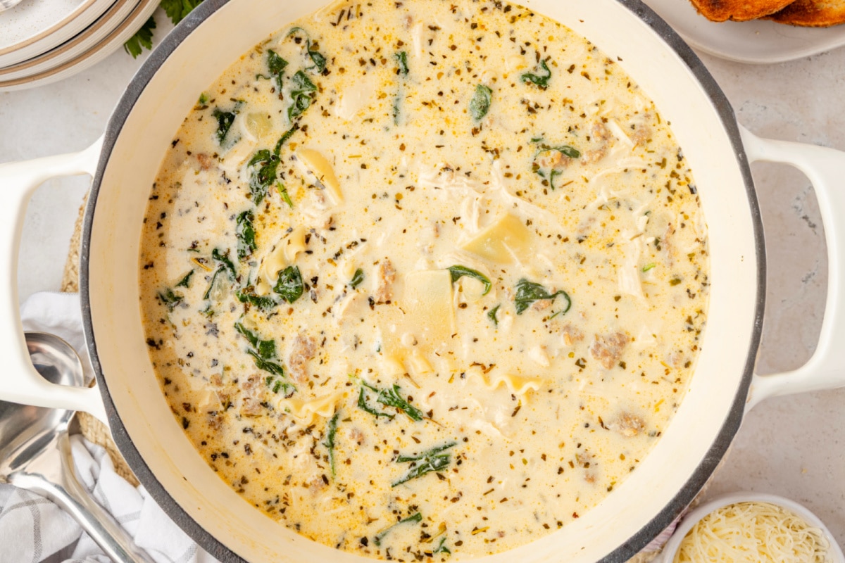 White Lasagna Soup with spinach, sausage, chicken, ricotta, and broken lasagna noodles simmering in a Dutch oven