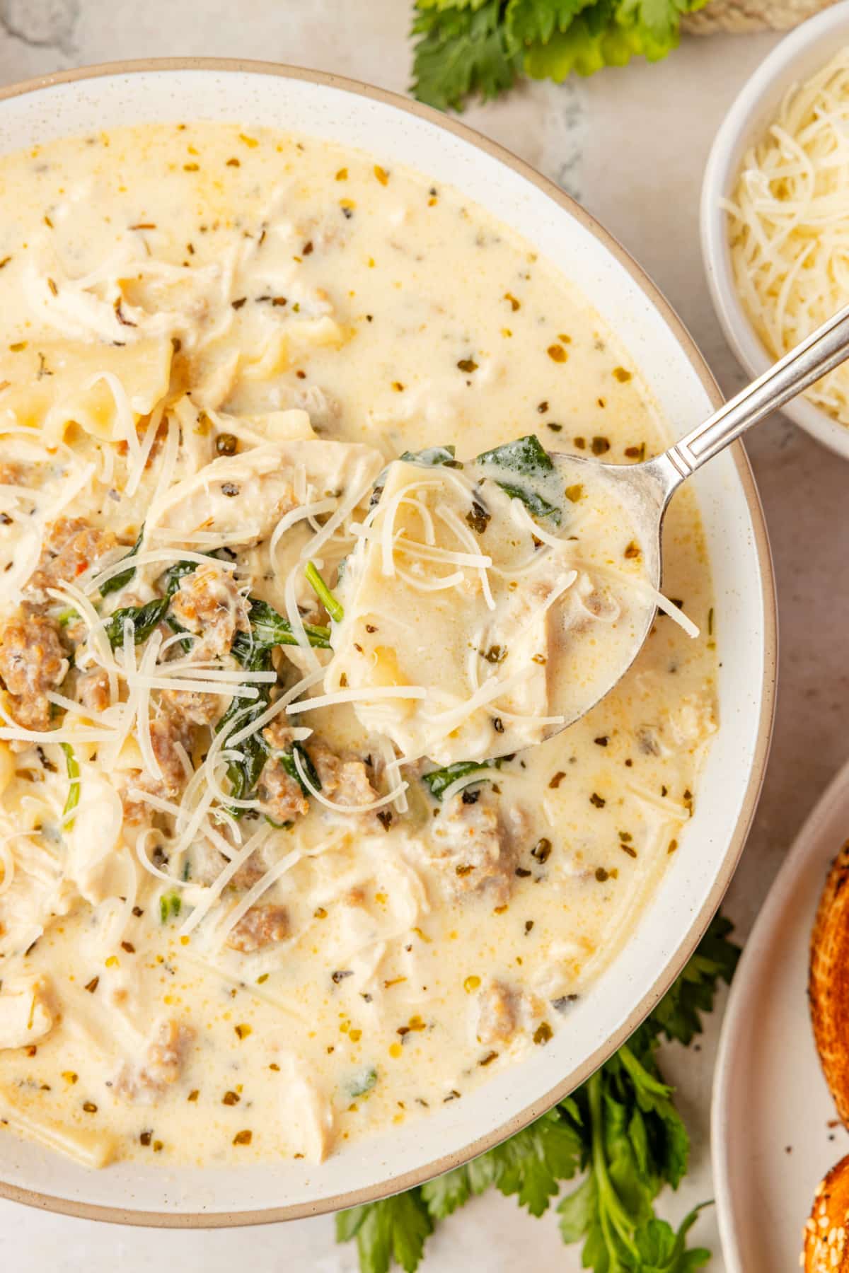 White Lasagna Soup with sausage, chicken, spinach, ricotta, and broken lasagna noodles in a creamy broth topped with Parmesan cheese