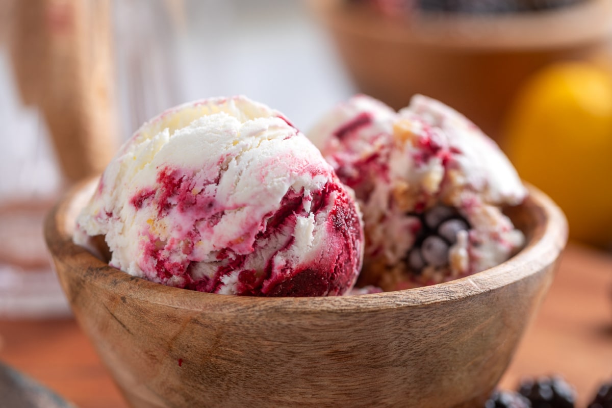 Two scoops of Blackberry Crumble à la Mode Ice Cream with thick blackberry ribbons in a wooden bowl.