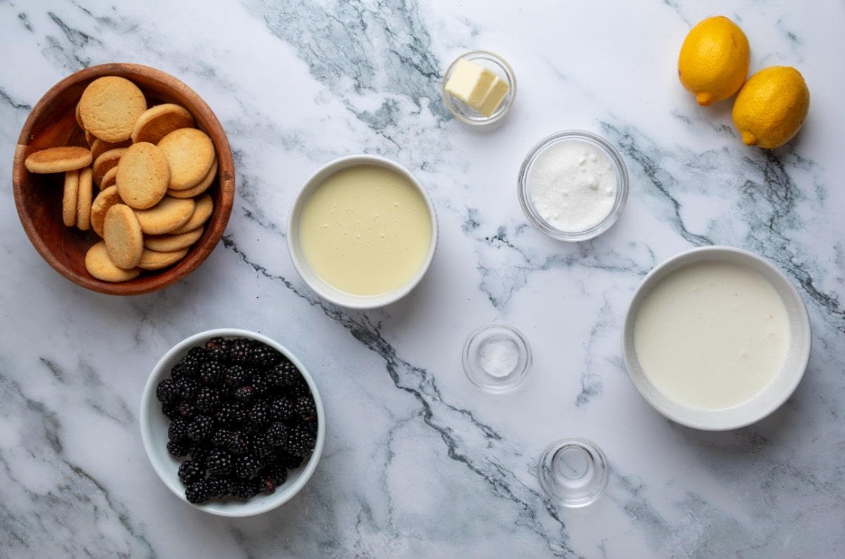 Ingredients for homemade no-churn blackberry ice cream including blackberries, heavy cream, sweetened condensed milk, shortbread cookies, lemons, butter, sugar, almond extract, and salt.