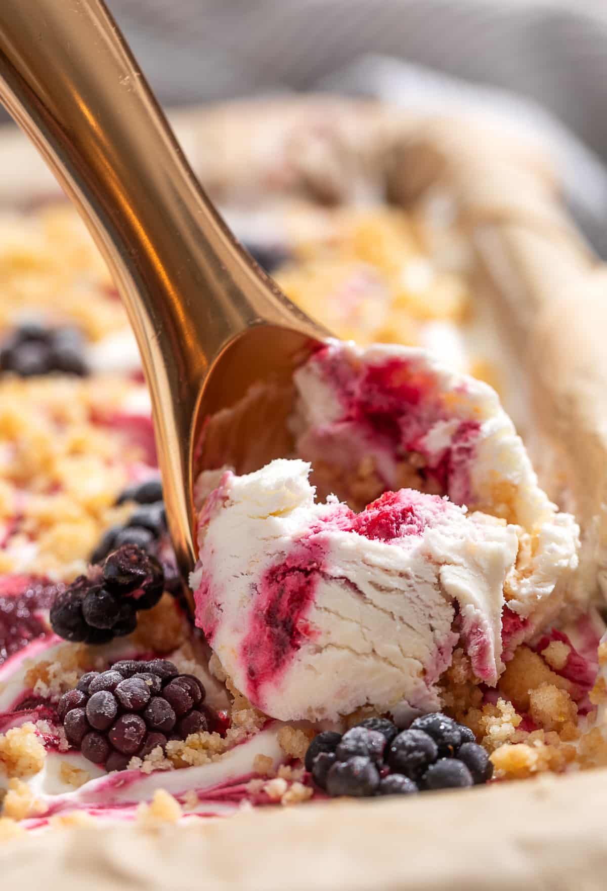 A scoop of homemade no-churn blackberry ice cream with blackberry swirls and buttery shortbread crumble being served from the loaf pan.