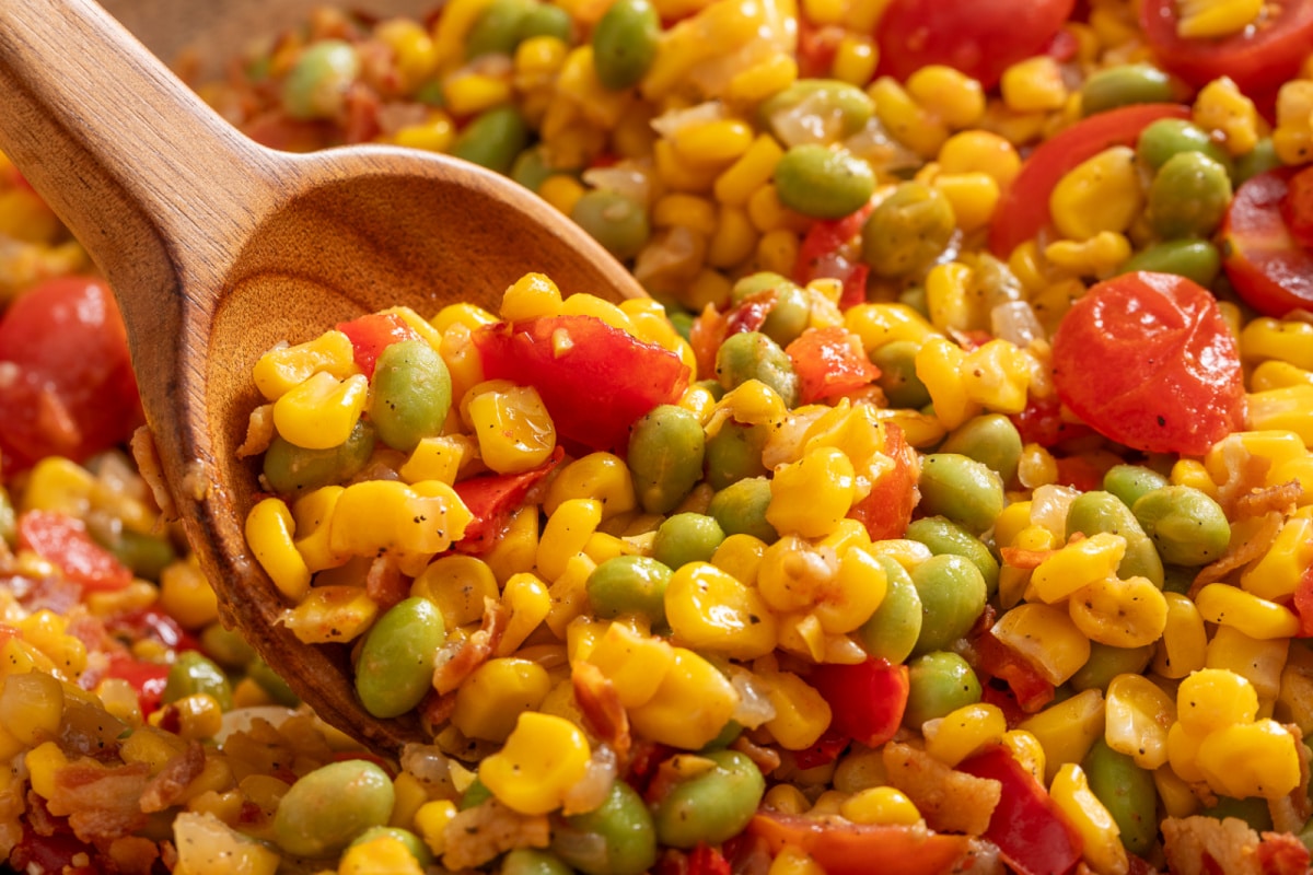 Close-up spoonful of corn succotash with edamame, tomatoes, bacon, and sweet corn
