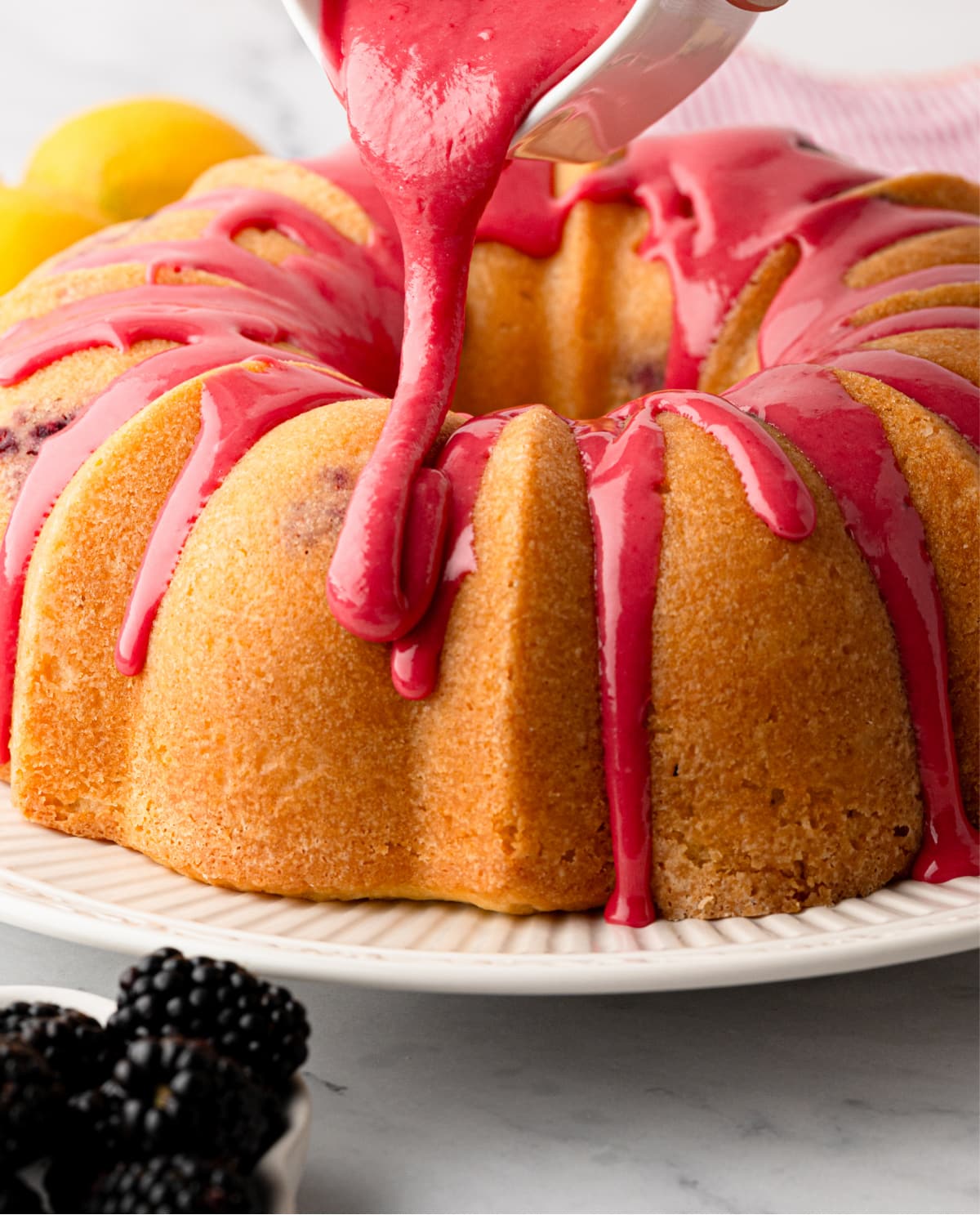 Fresh blackberry glaze being poured over a lemon Bundt cake