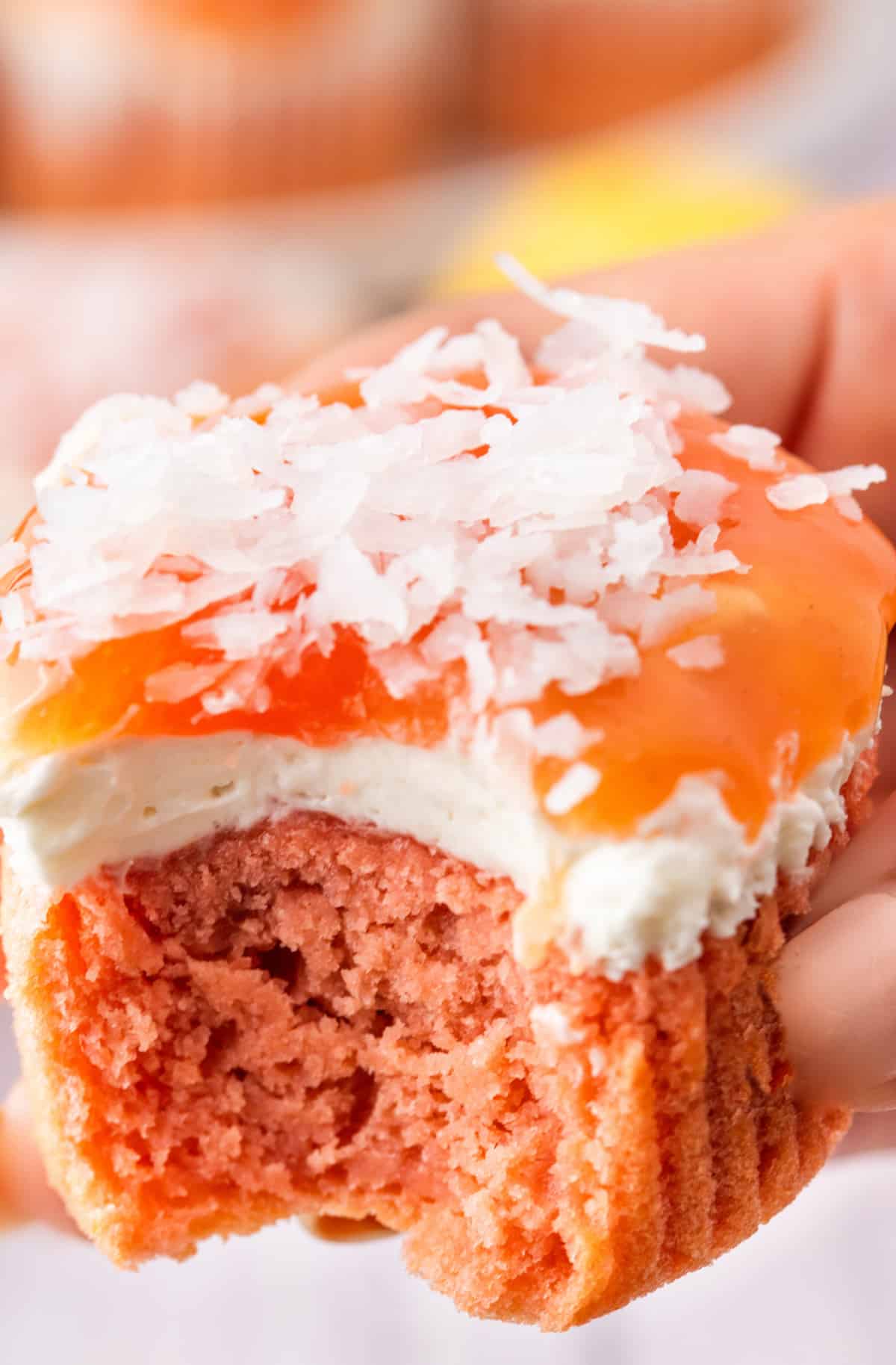A close look inside the cupcake shows the soft pink cake, creamy topping, and glossy guava glaze. Inside of a guava cream cheese cupcake showing the pink cake, cream cheese layer, guava glaze, and coconut