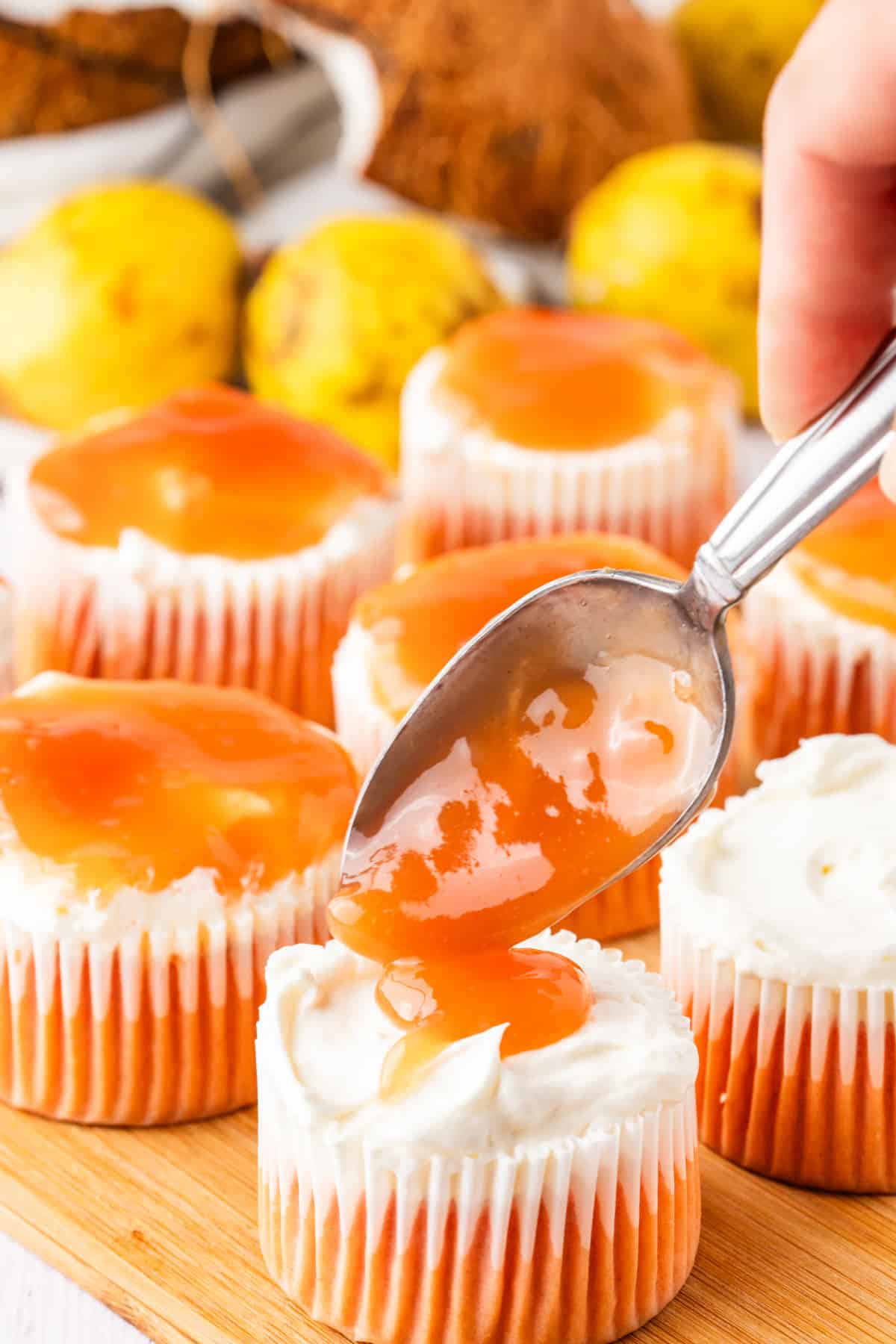 The cooled guava glaze gets spooned over the cream cheese layer to create the signature topping. Spooning guava glaze over cream cheese topped cupcakes before adding coconut