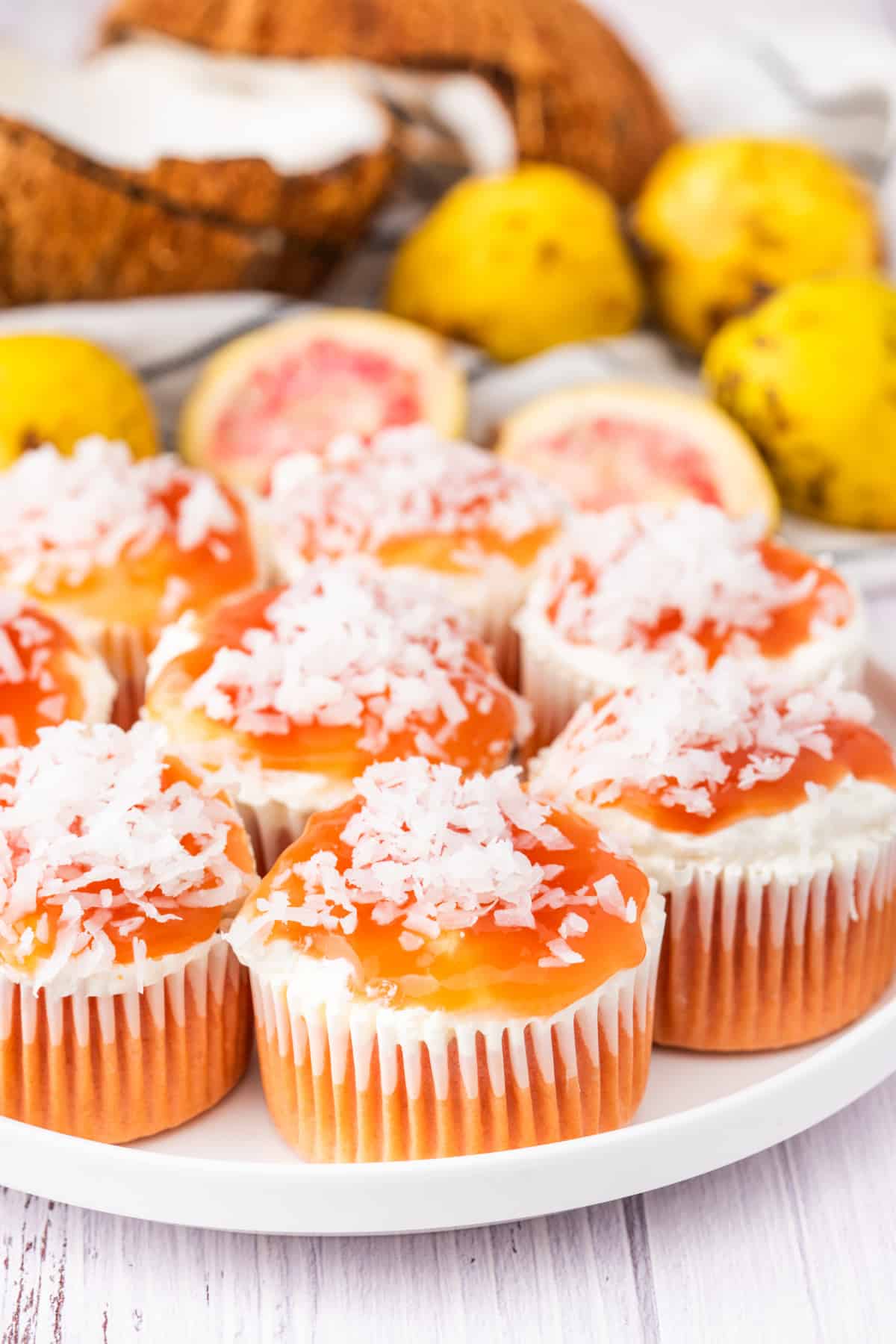 A platter of guava glazed cream cheese cupcakes finished with coconut and glossy guava topping. Plate of guava glazed cream cheese cupcakes topped with coconut and guava glaze