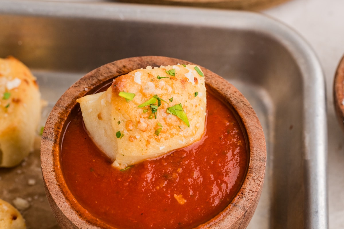 Parmesan bread bite dipped in marinara sauce and topped with Parmesan cheese and parsley