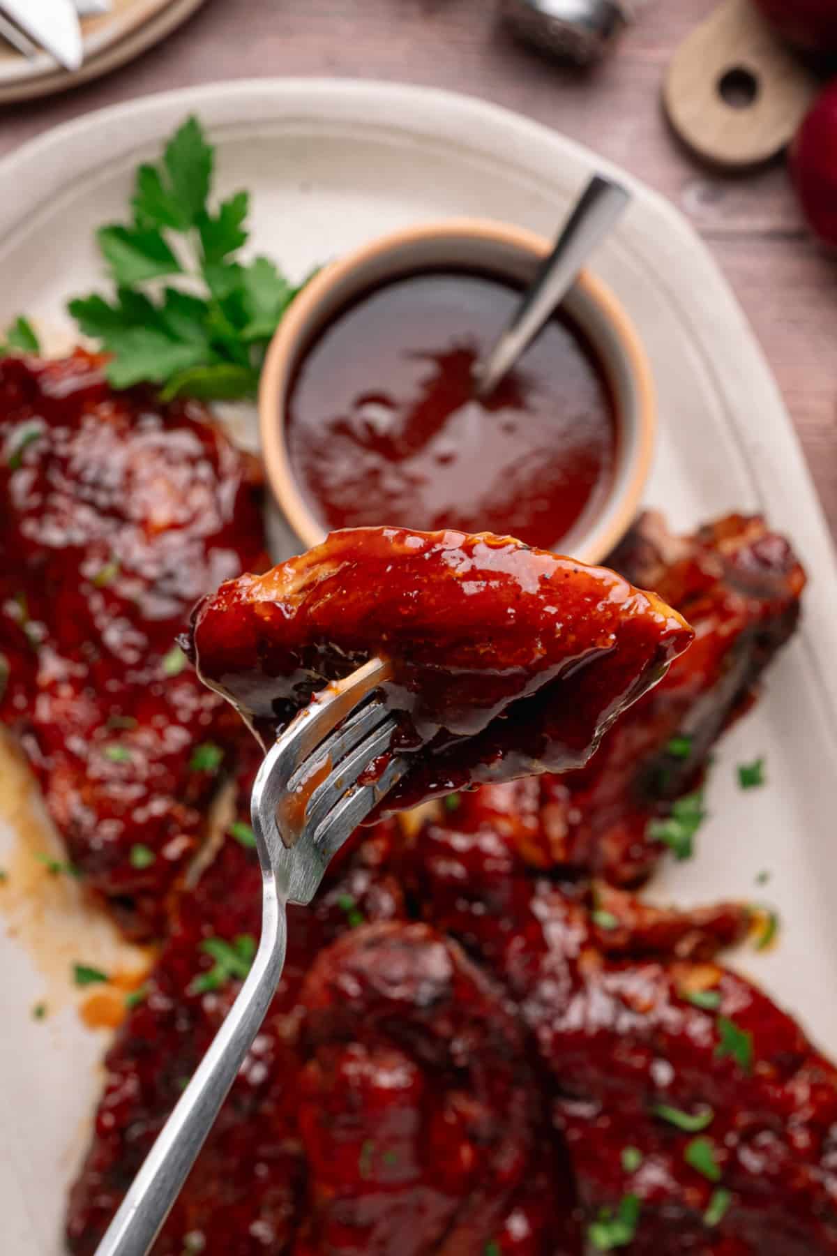 Fork lifting a peach bourbon glazed country style rib over a platter of ribs with sauce in a bowl