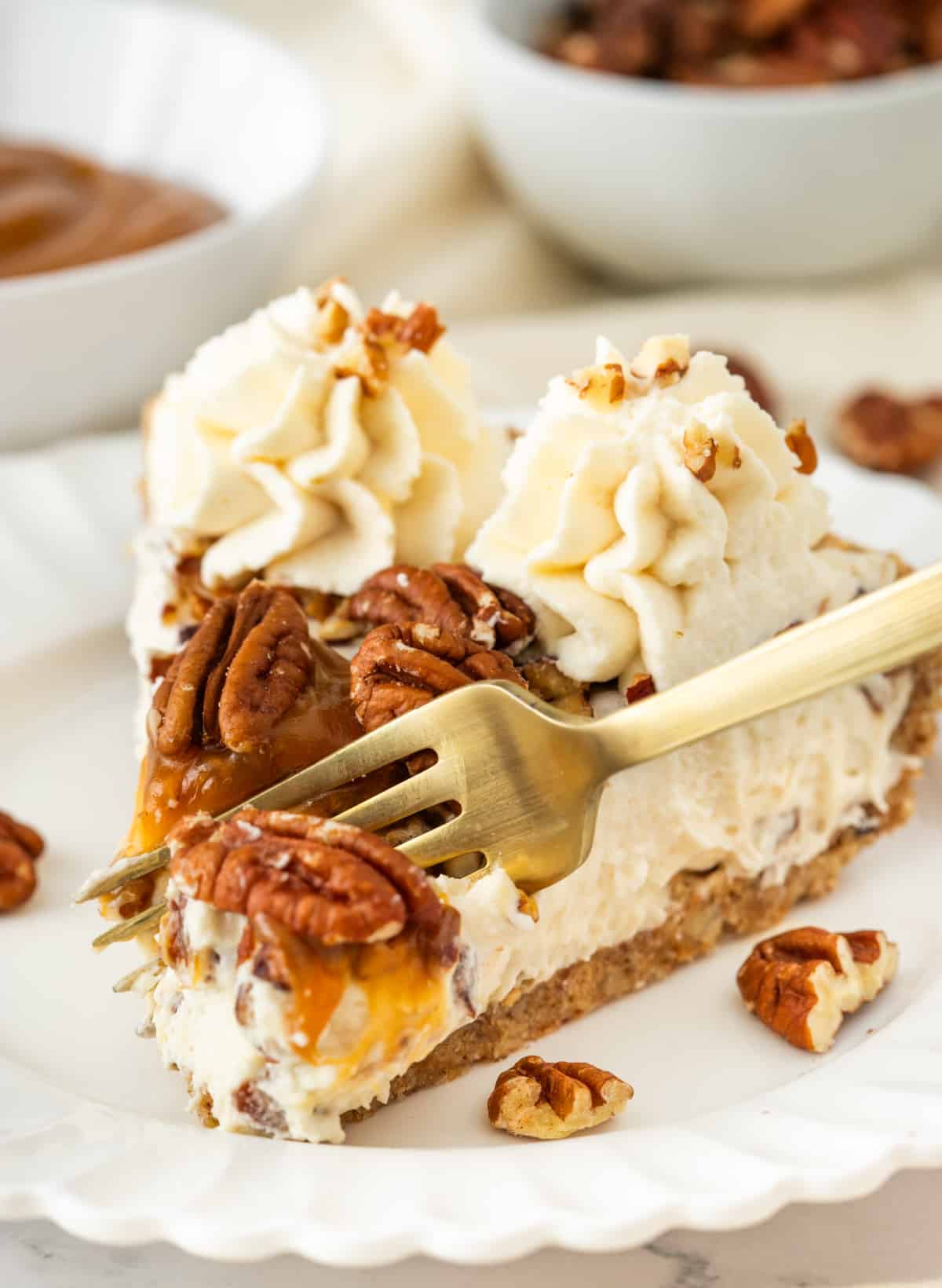 Fork lifting a bite of pecan cream pie with toasted pecans, caramel drizzle, whipped cream, and pecan crust