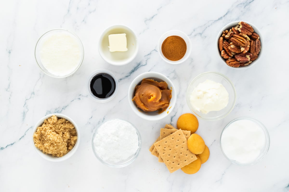 Ingredients for pecan cream pie including pecans, cream cheese, heavy cream, graham crackers, vanilla wafers, brown sugar, powdered sugar, and vanilla
