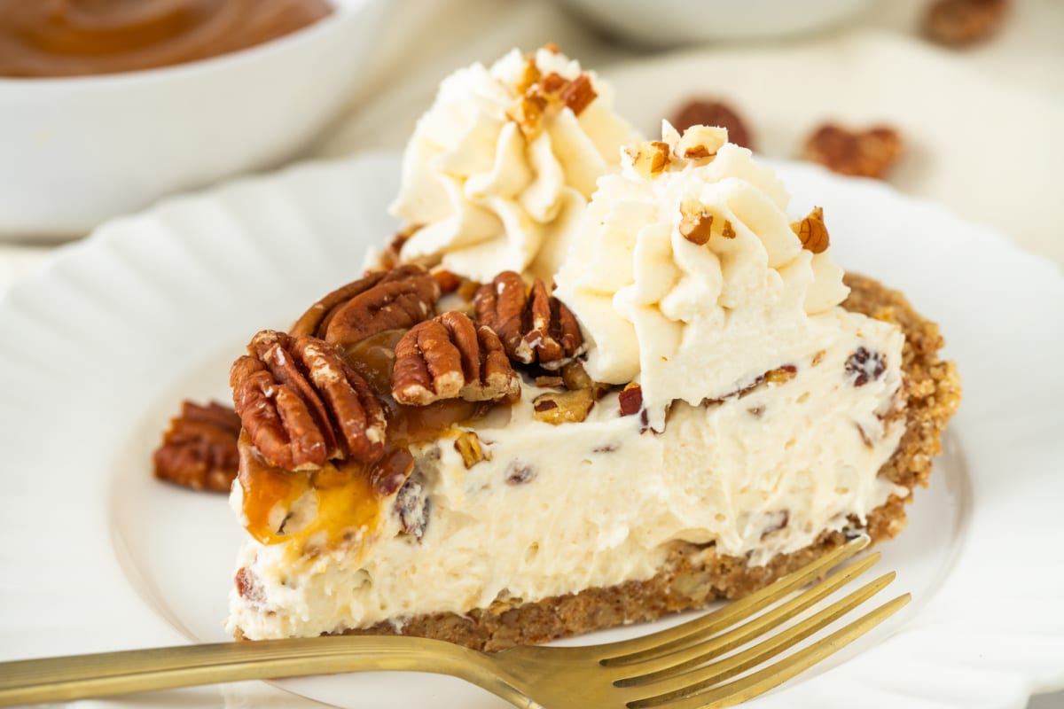 Close-up slice of pecan cream pie with toasted pecans, whipped cream, caramel drizzle, and pecan crust