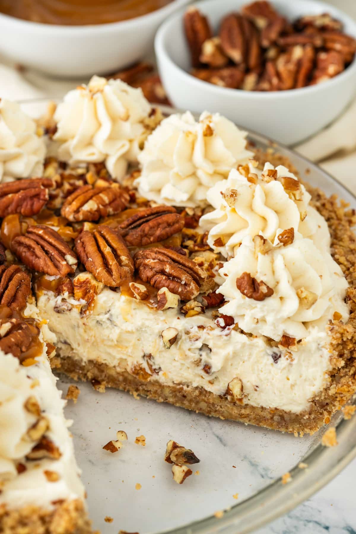 Pecan cream pie with a slice removed, showing the toasted pecan filling, pecan crust, whipped cream, and caramel topping