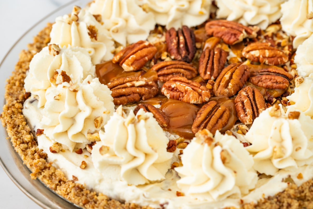 Whole pecan cream pie topped with whipped cream, toasted pecans, caramel drizzle, and a pecan crust