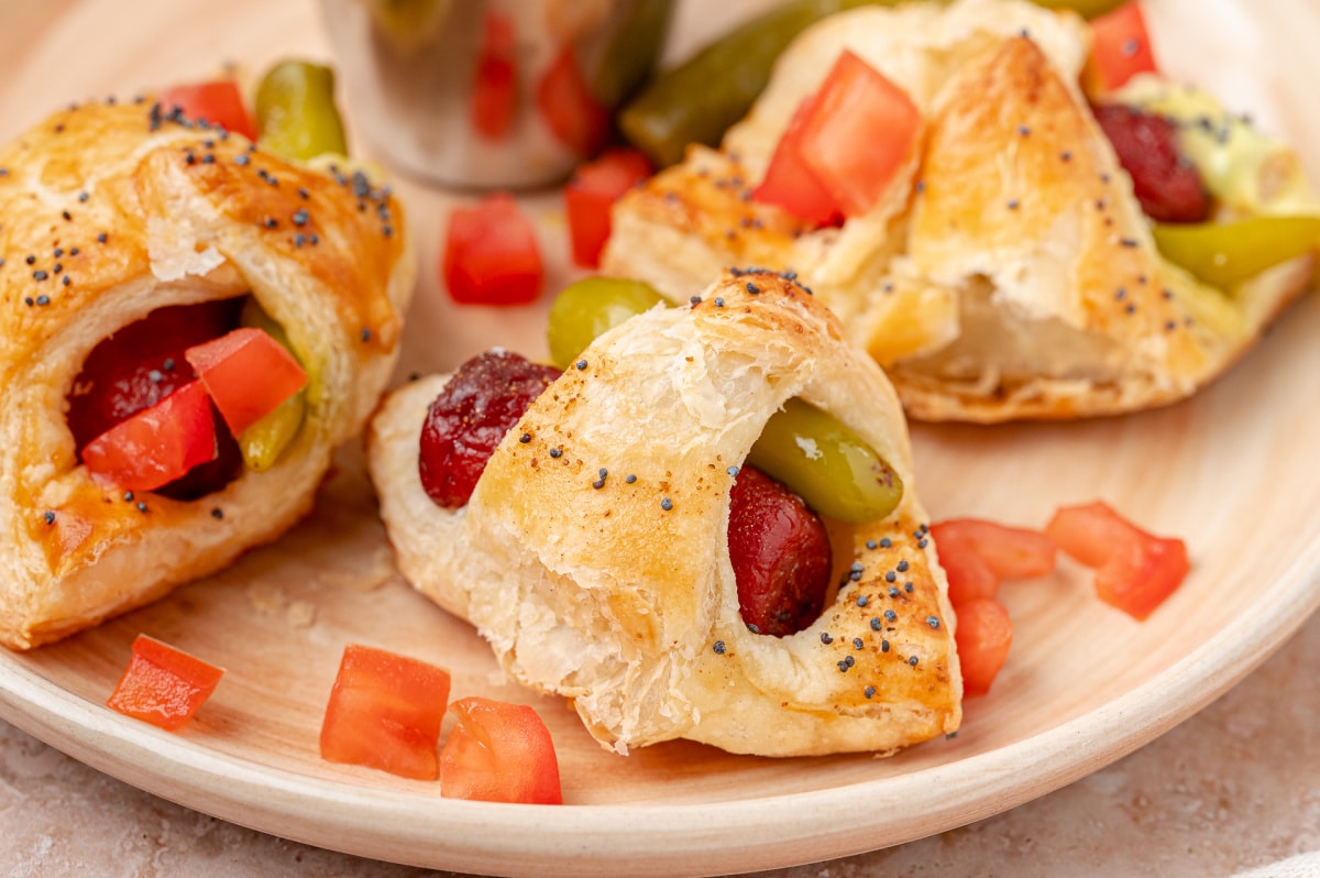 Close-up of flaky puff pastry wrapped around a beef cocktail frank and sport pepper.