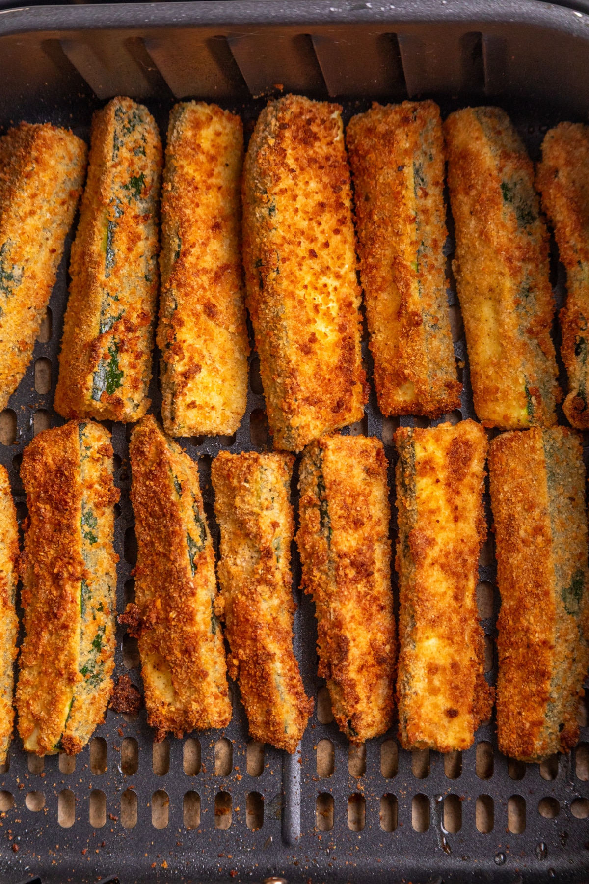Breaded zucchini fries cooking in an air fryer basket until crisp and golden.