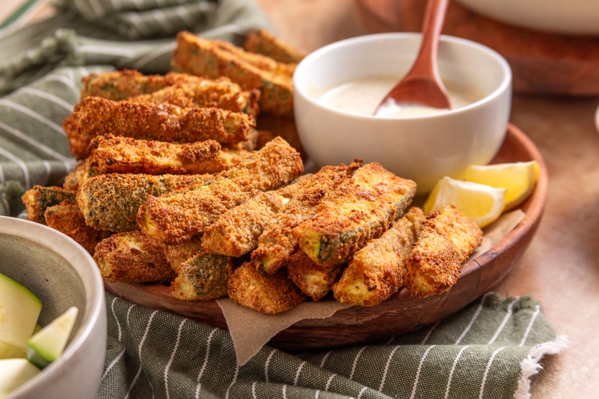 Serving platter of air fryer zucchini fries with homemade lemon garlic aioli and lemon wedges.