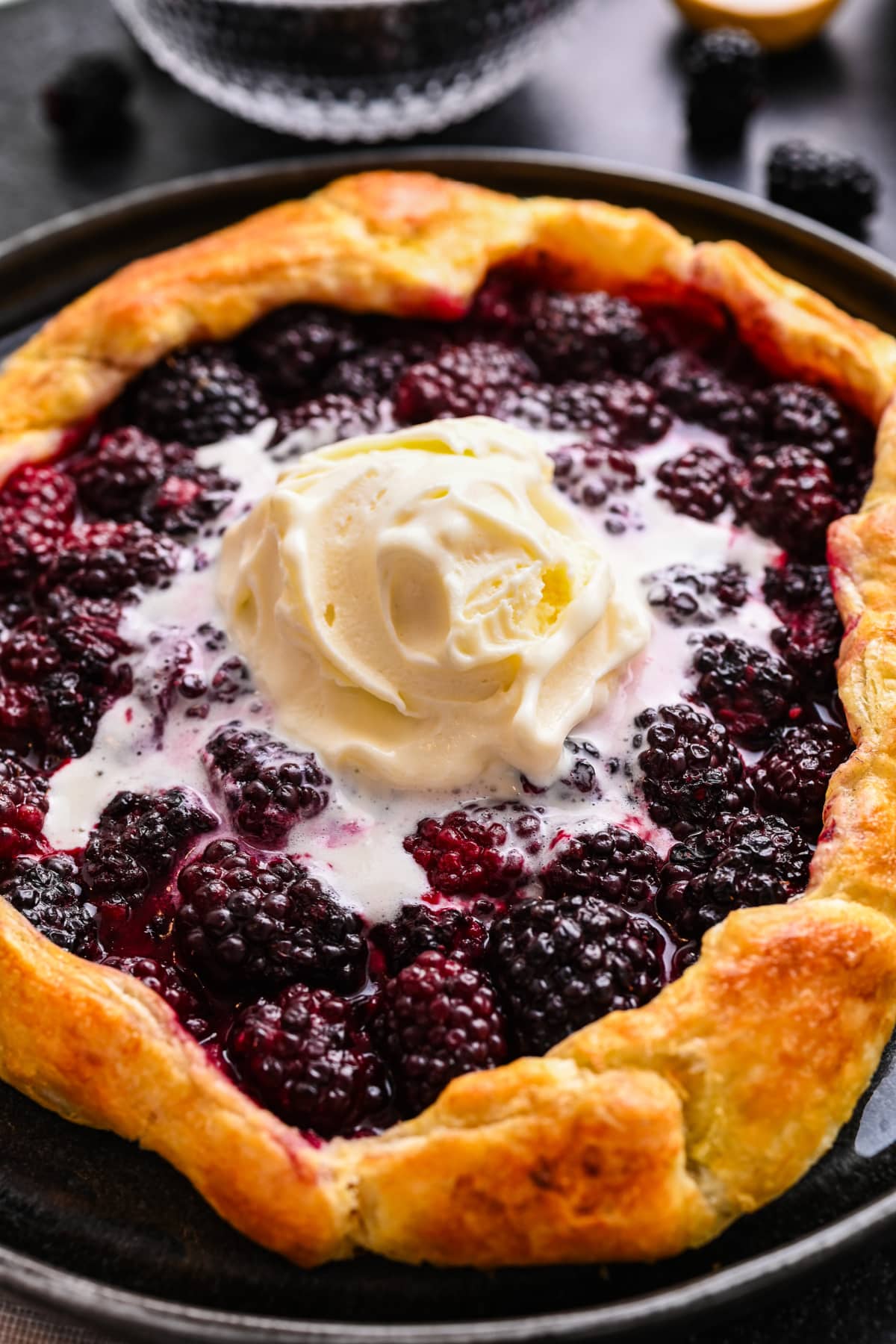 Close-up of blackberry puff pastry galette served warm with vanilla ice cream.