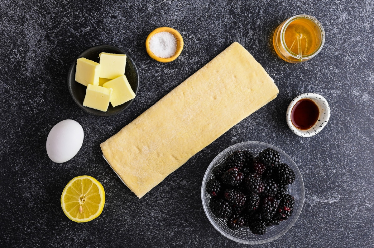 Ingredients for blackberry puff pastry galette including fresh blackberries, puff pastry, honey, butter, lemon, vanilla, egg, and salt.