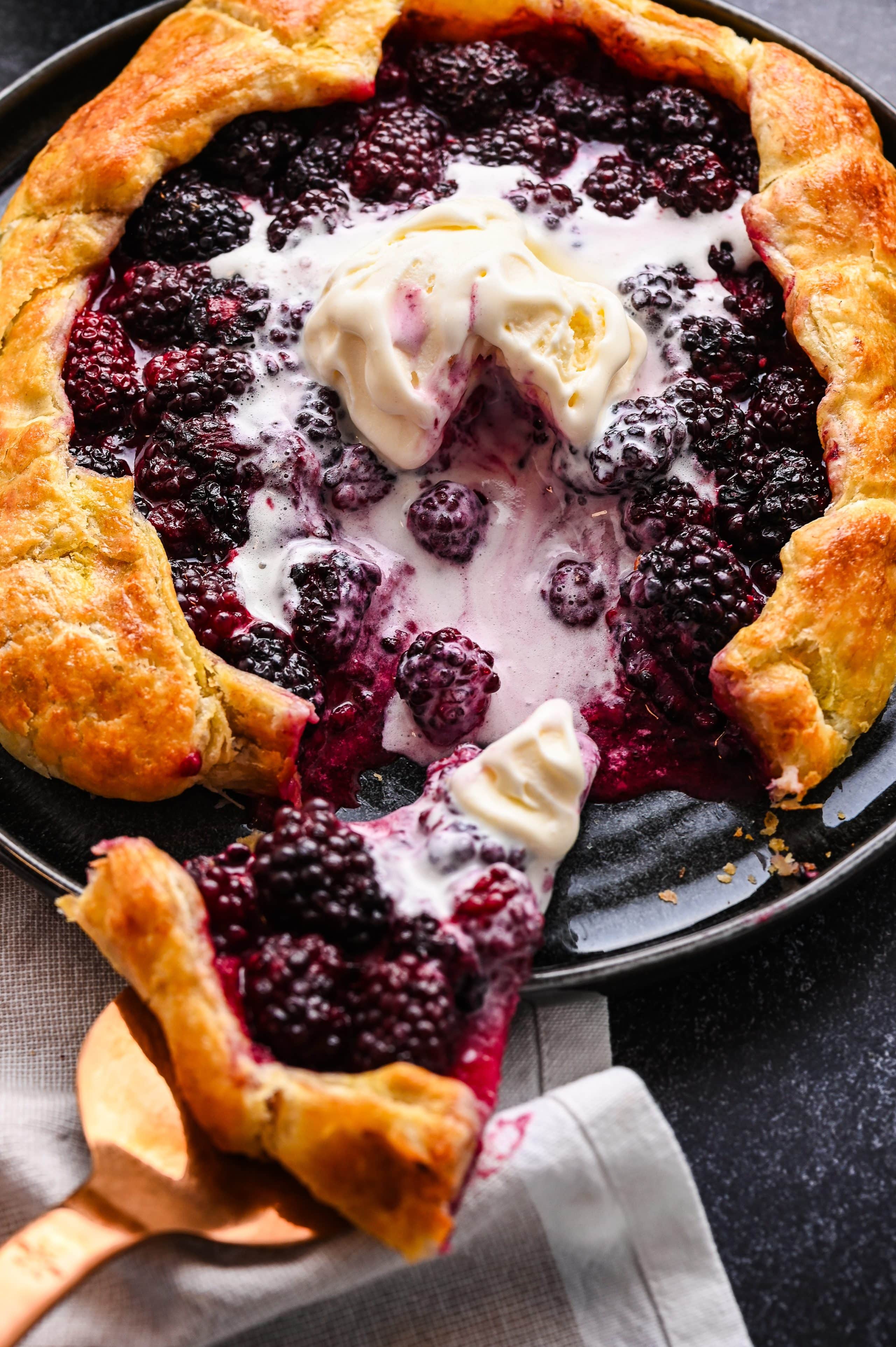 Serving a slice of blackberry puff pastry galette with vanilla ice cream.