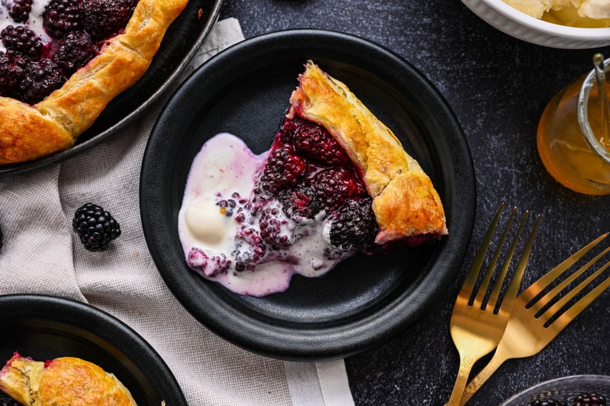 Slice of blackberry puff pastry galette served with melting vanilla ice cream.