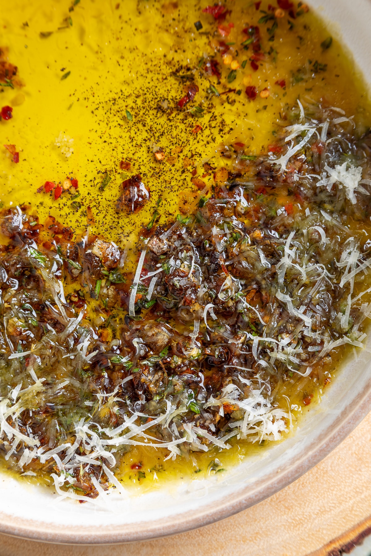 Close-up of bread dipping oil with caramelized shallots, Parmesan, fresh herbs, and cracked black pepper.