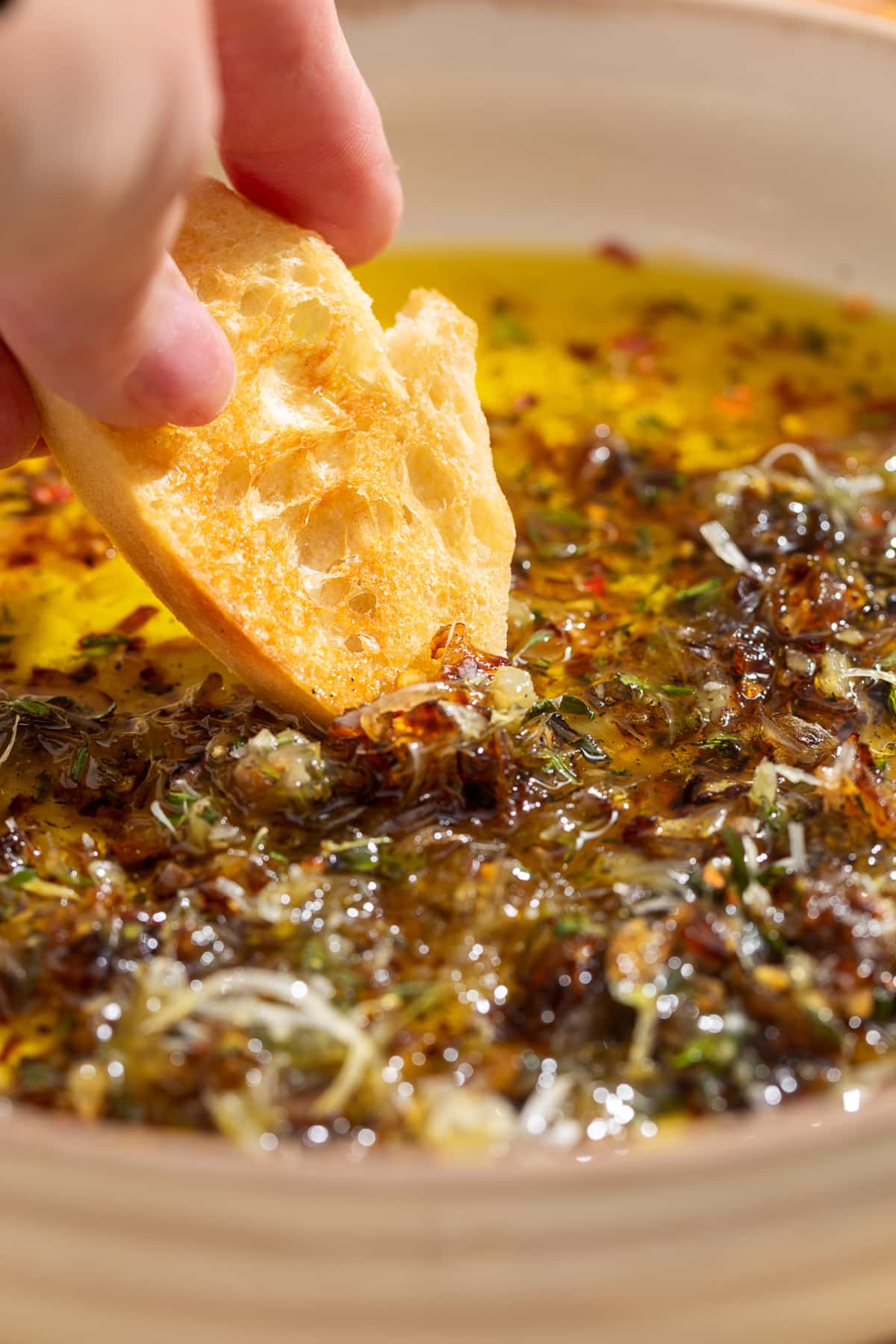 Toasted bread dipping into bread dipping oil with caramelized shallots, fresh herbs, and Parmesan.