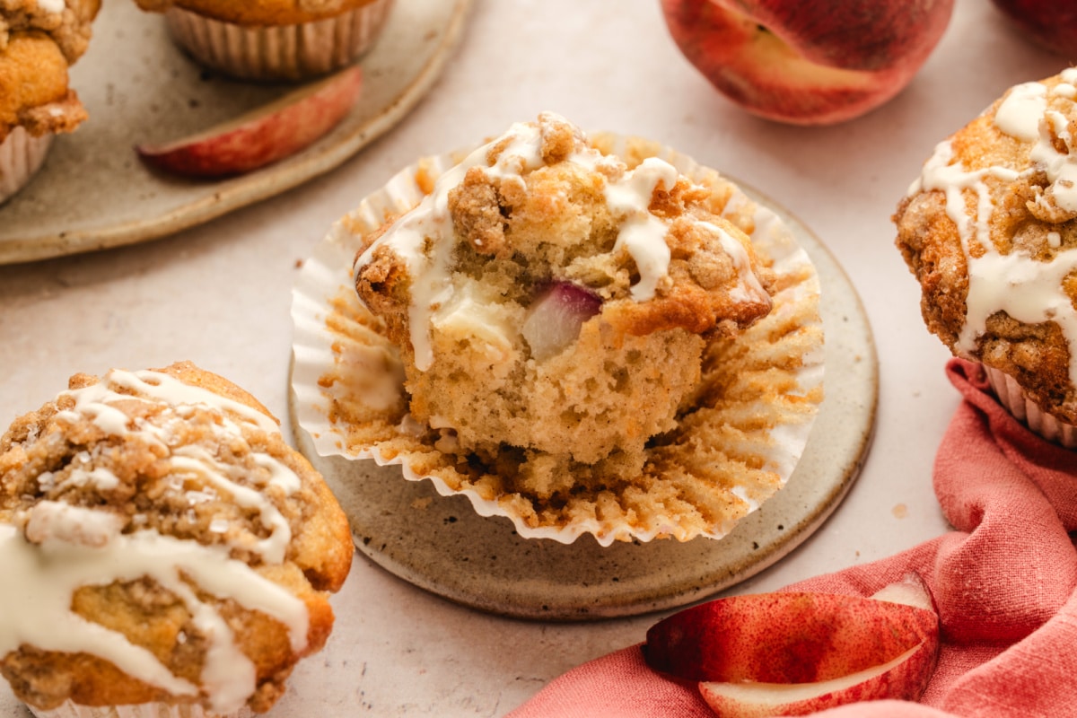 Fresh peach pieces inside a brown butter peach coffee cake muffin Inside of a brown butter peach coffee cake muffin showing fresh peach pieces, cinnamon streusel, and vanilla glaze