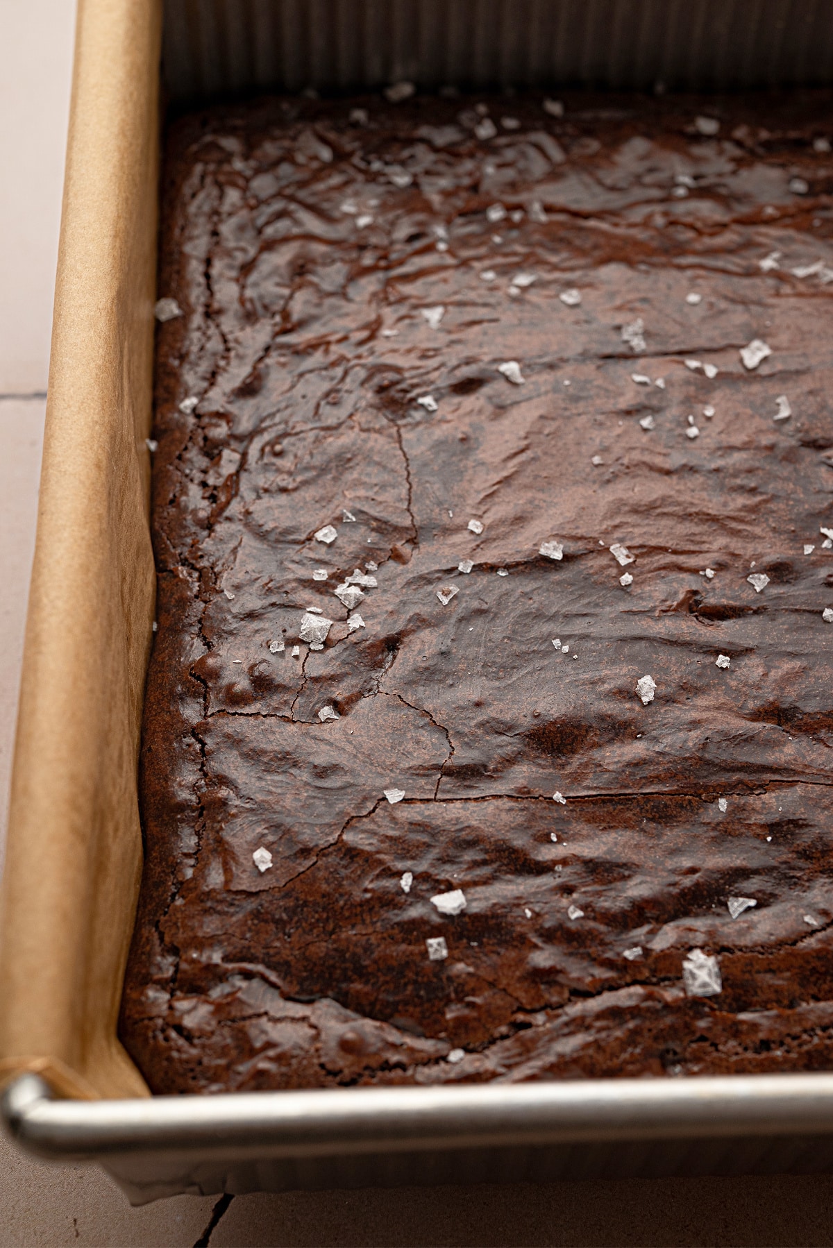 Freshly baked Cabernet Sauvignon brown butter brownies in a parchment-lined baking pan with flaky sea salt.