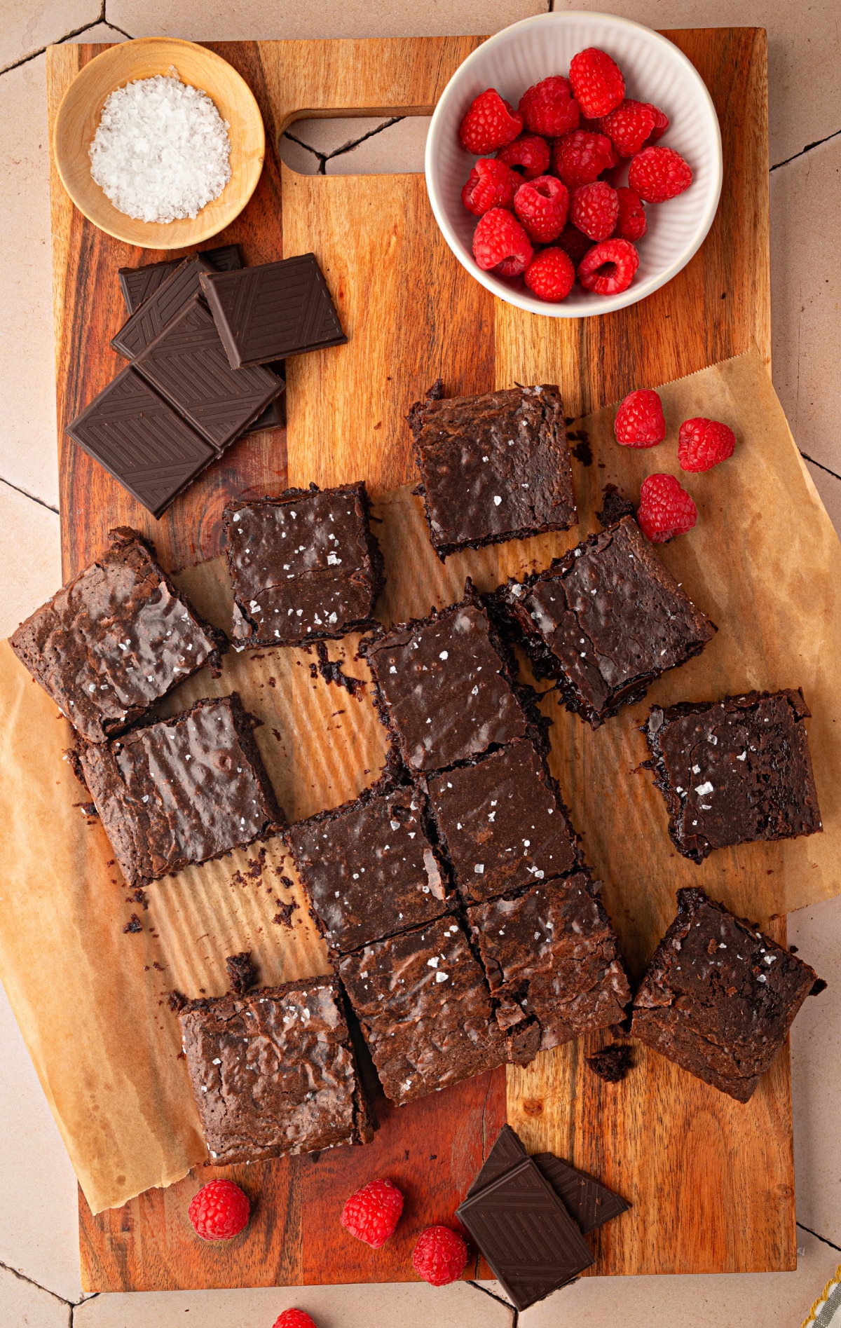 Cabernet Sauvignon brown butter brownies arranged on a wooden serving board with dark chocolate, flaky sea salt, and fresh raspberries.