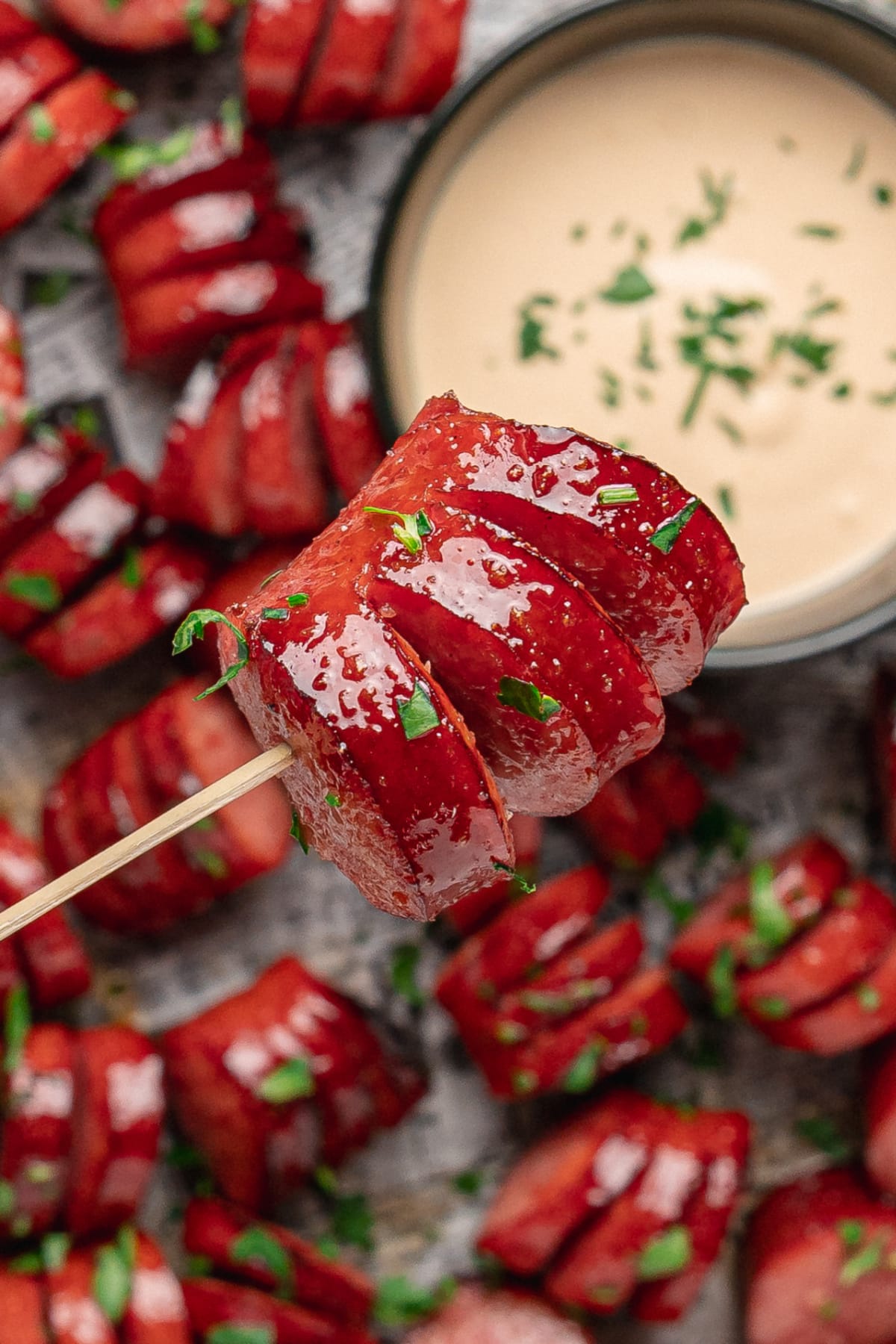 Close-up of a glazed honey garlic kielbasa bite on a skewer with creamy honey mustard.