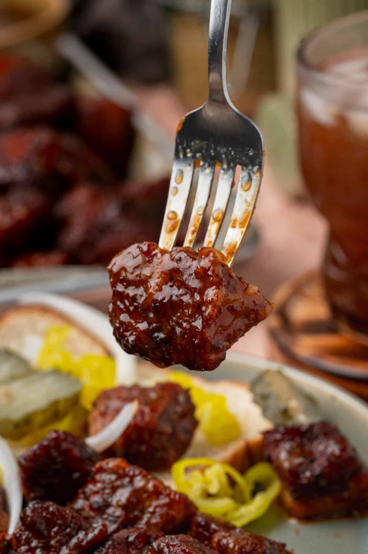 Close-up of a caramelized pork belly burnt end coated in glossy peach tea glaze on a fork.