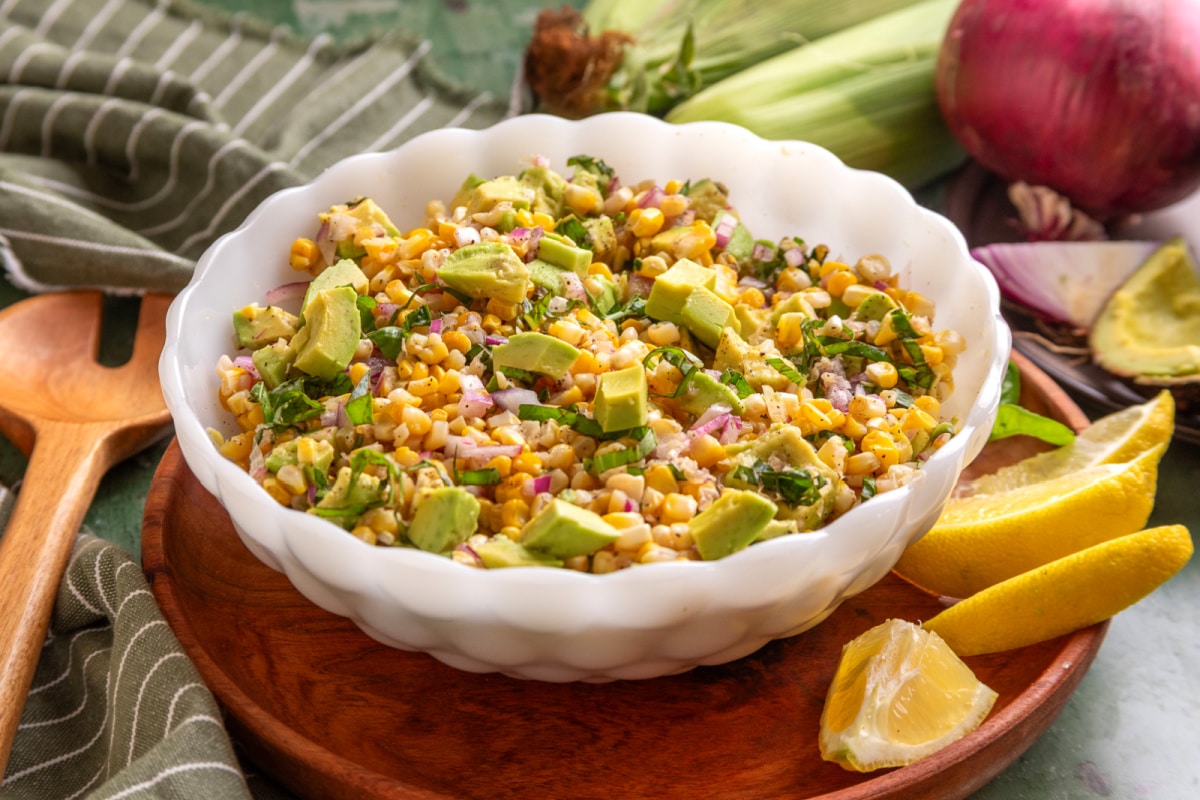 Serving bowl of grilled corn salad with avocado and basil tossed with red onion and a lemon vinaigrette.