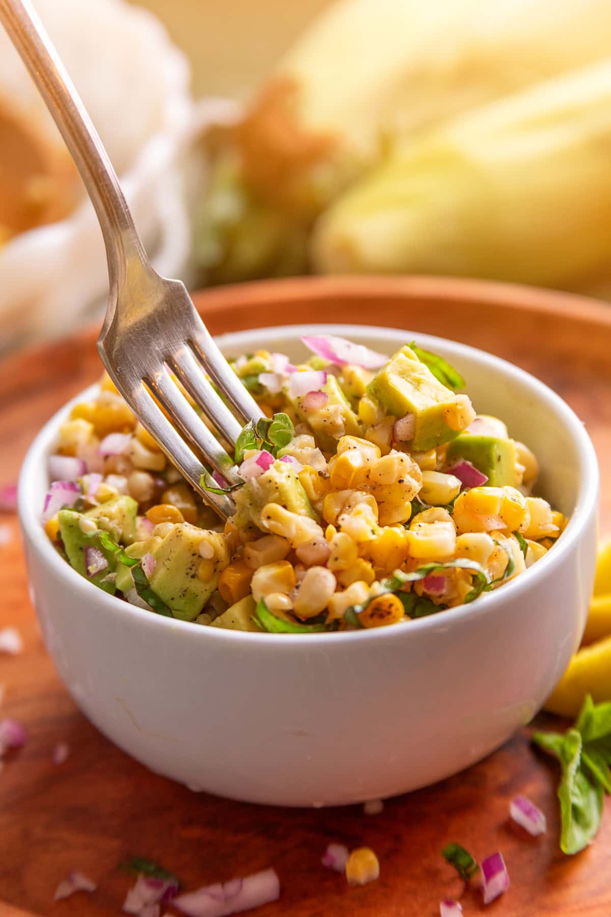 Fork lifting a bite of grilled corn salad with avocado, basil, and red onion.