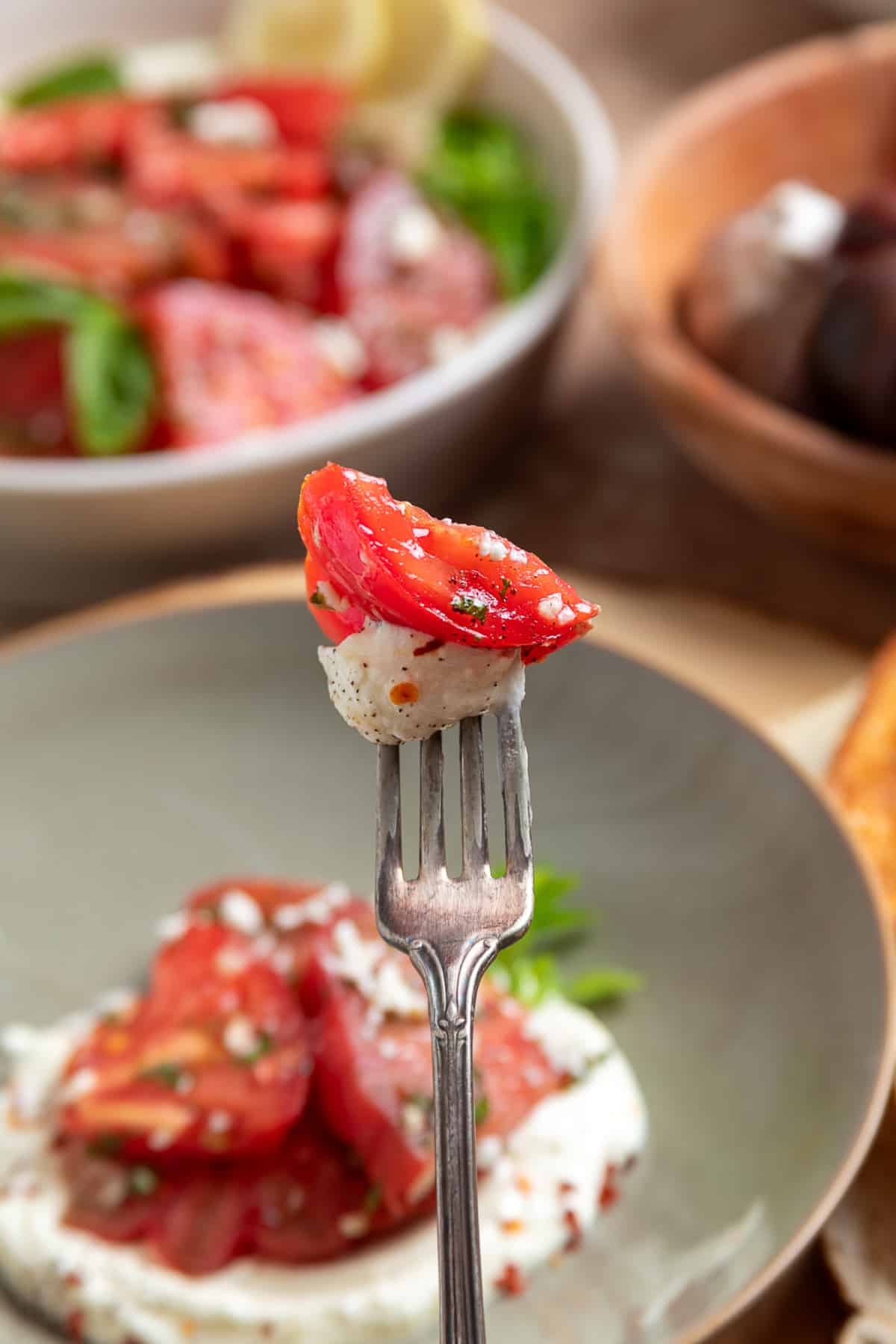 Forkful of heirloom tomato salad with creamy whipped ricotta feta, fresh basil, and lemon vinaigrette.